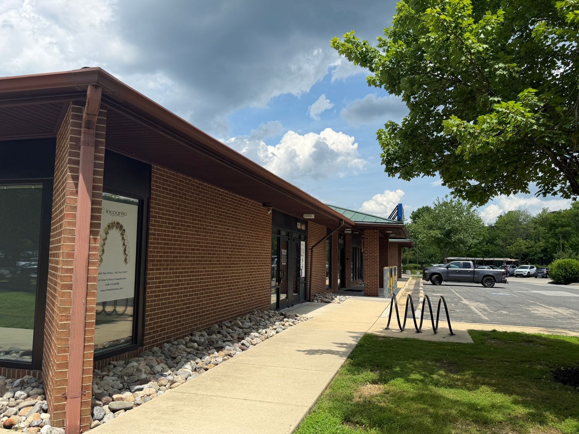 Brick building exterior with sidewalk, tree, and parking lot under a partly cloudy sky