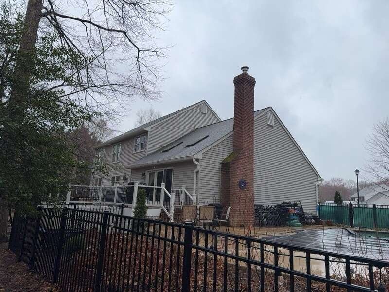 Suburban house with brick chimney and black fence in a snowy yard under a cloudy sky