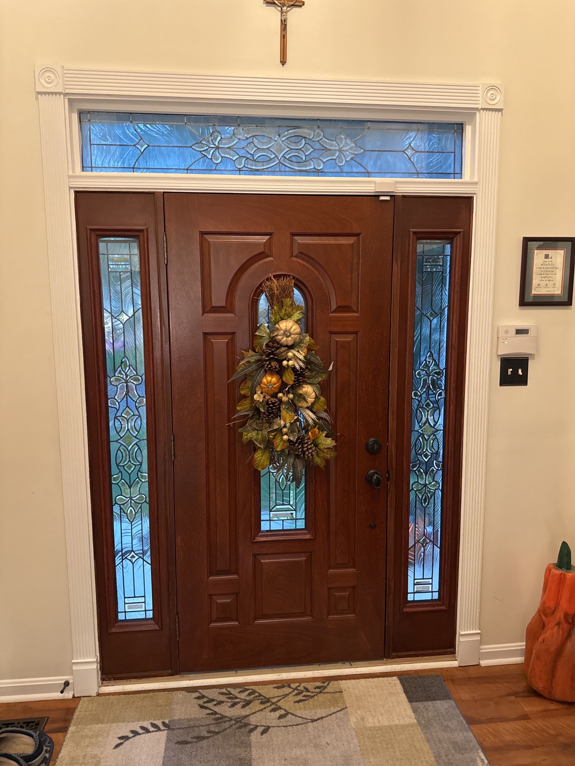 Wooden front door with stained glass sidelights and a wreath, viewed from inside a home.
