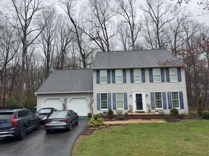 Suburban two-story house with gray siding, blue shutters, two cars in the driveway, and leafless trees behind