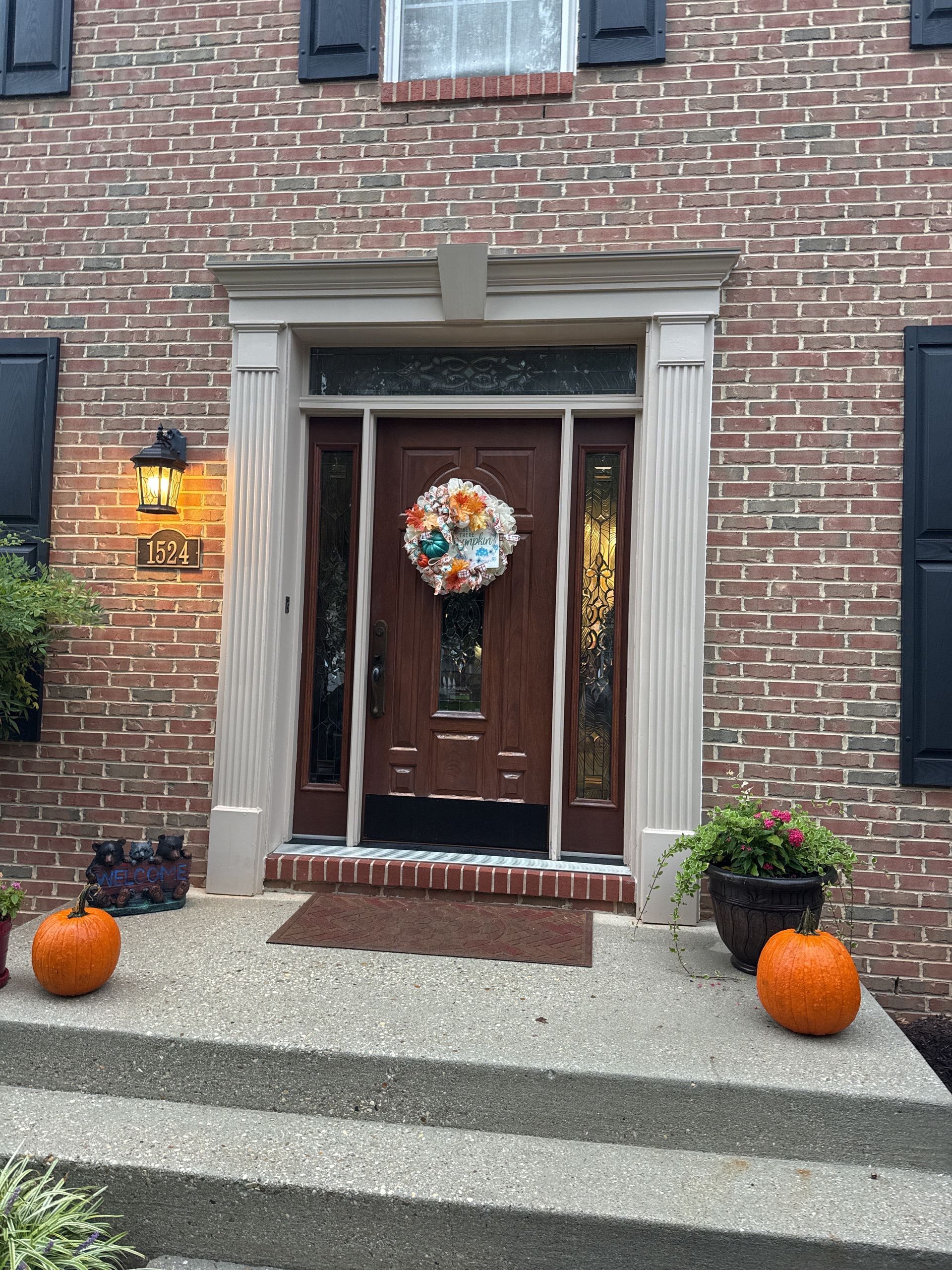 Brick townhouse entrance with wooden door, fall wreath, pumpkins, and potted plants by the steps