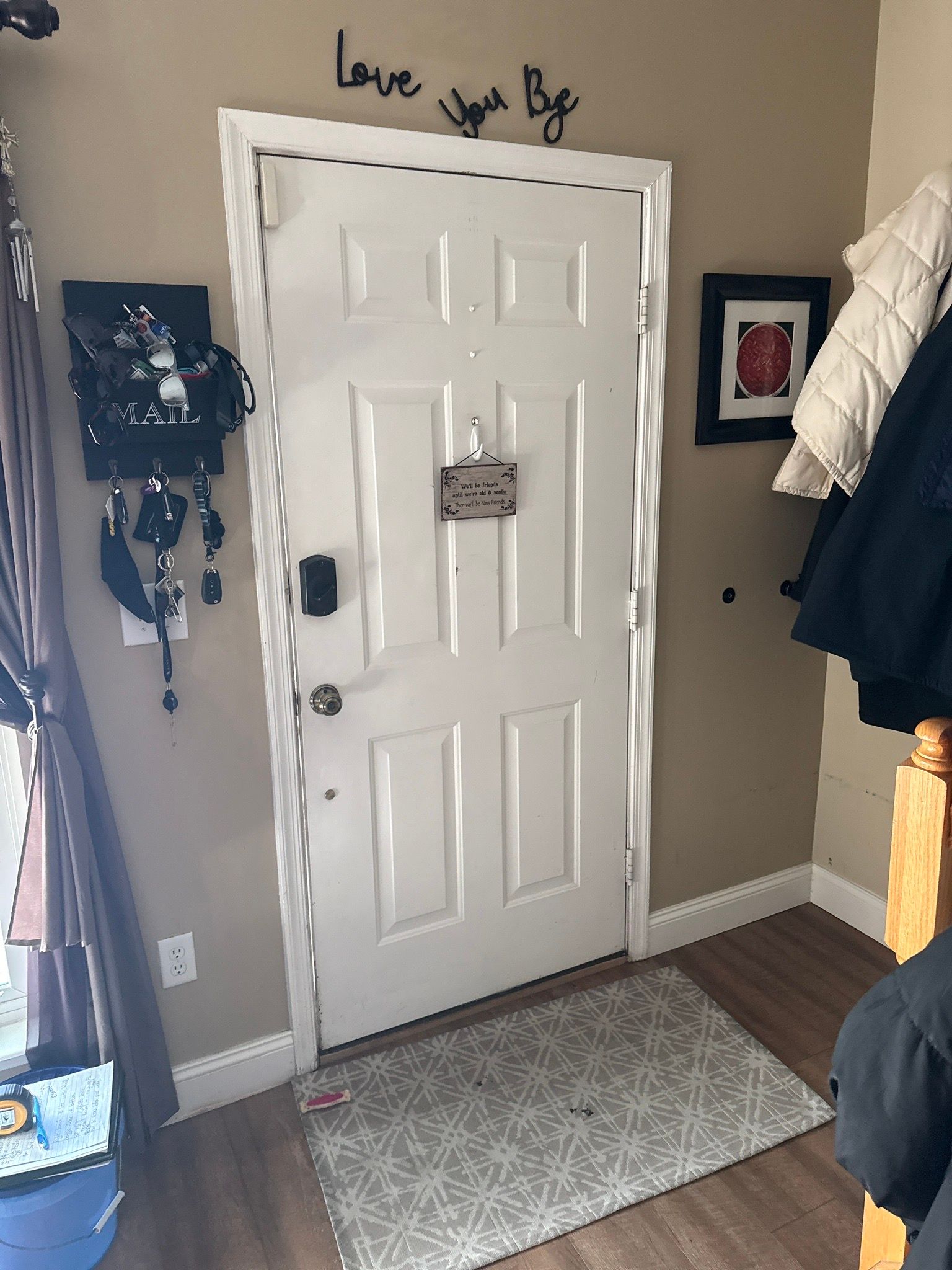 Front door with gray rug, wall decor, and hanging coats in a small entryway.
