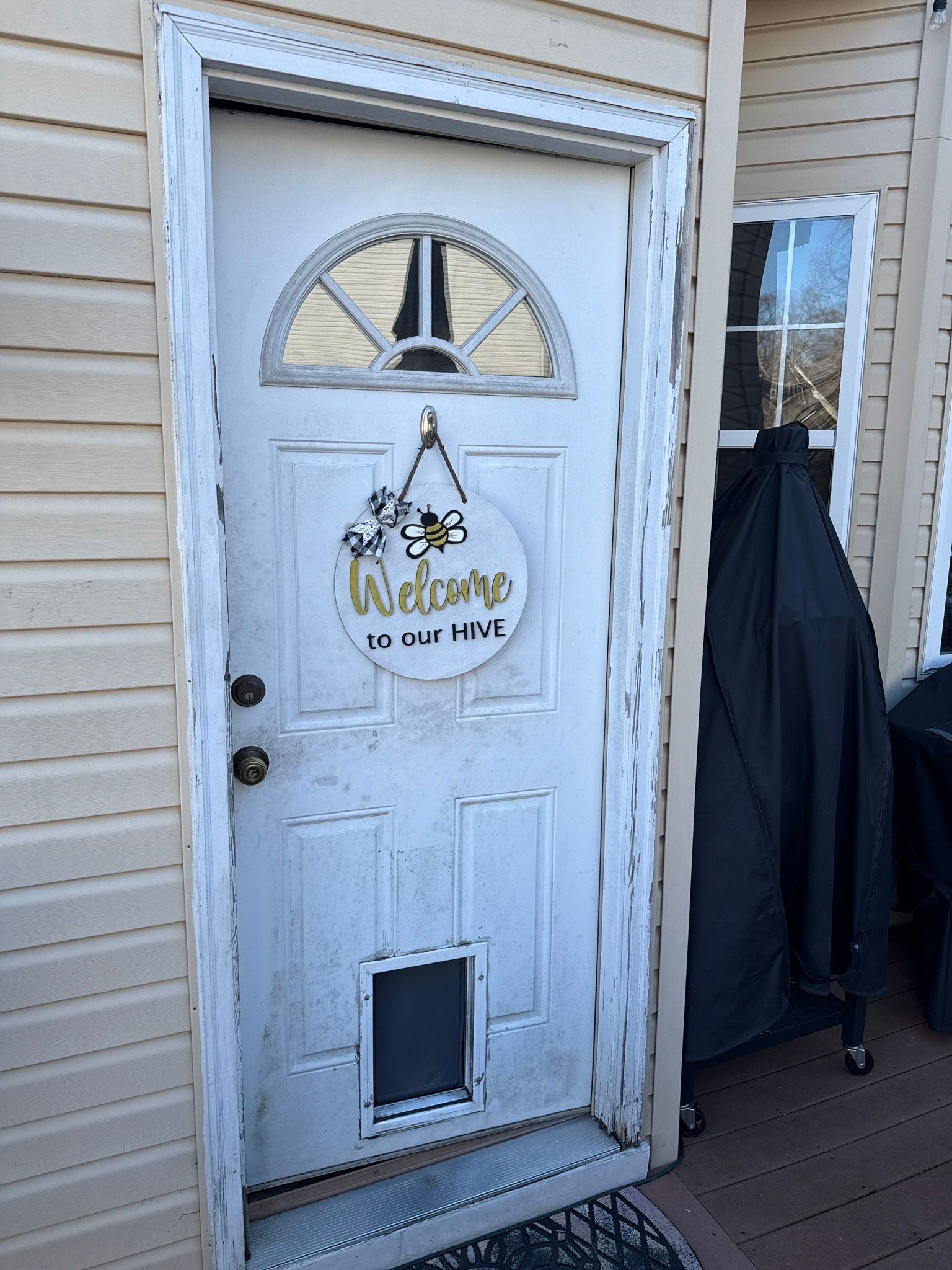 White front door with “Welcome” sign, pet door, and hanging coats beside it.