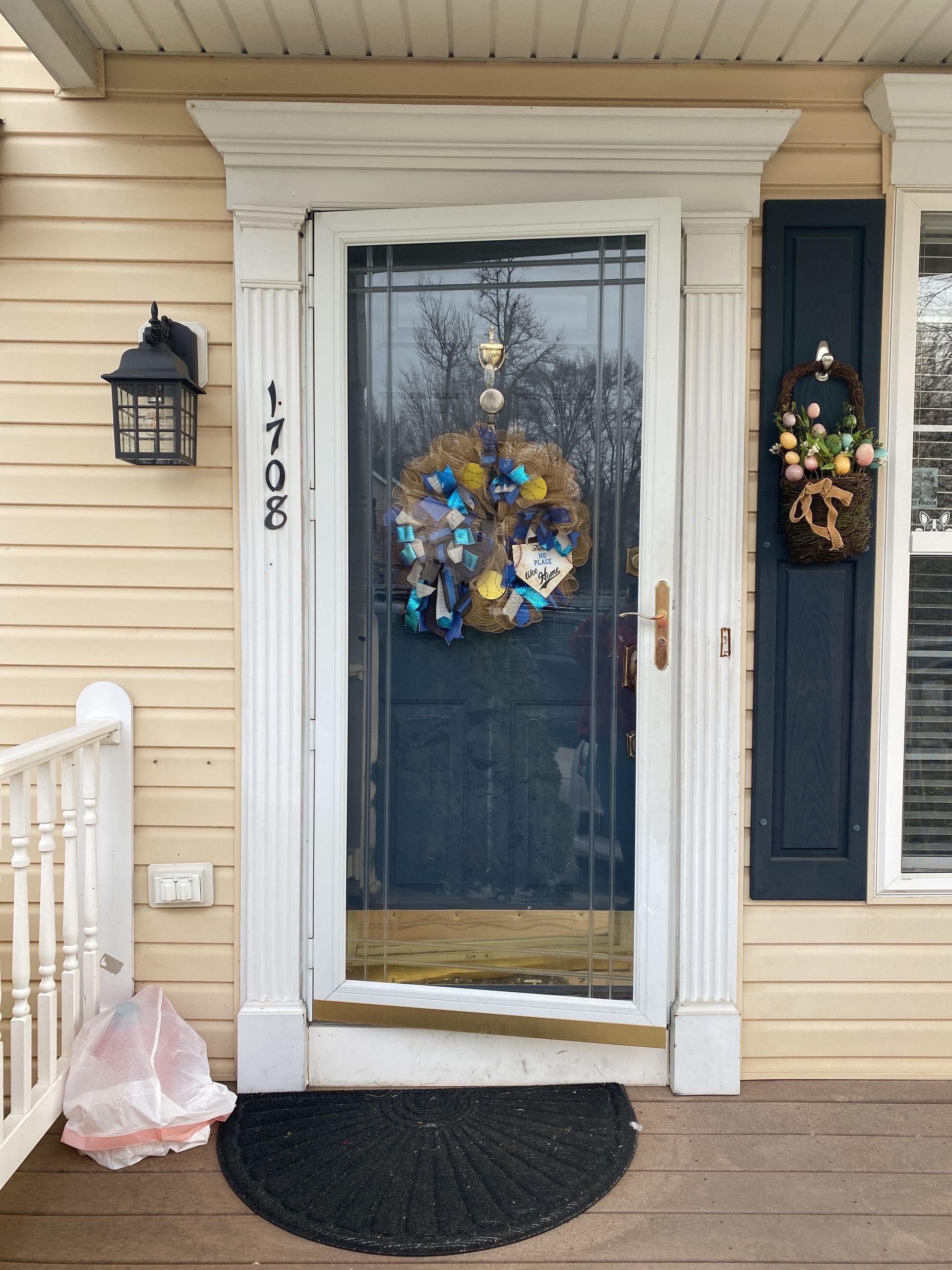 Front door with blue wreath, white trim, black lantern, and pink sandbag by the steps