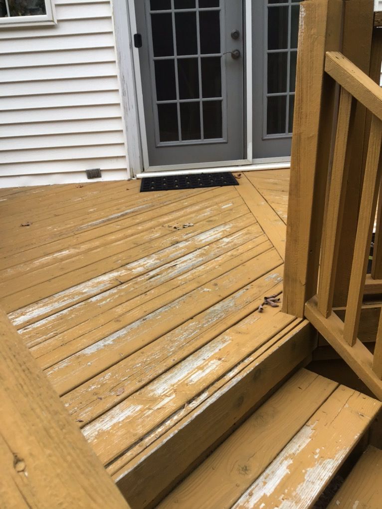Wooden deck with white paint peeling near a back door and steps beside a railing
