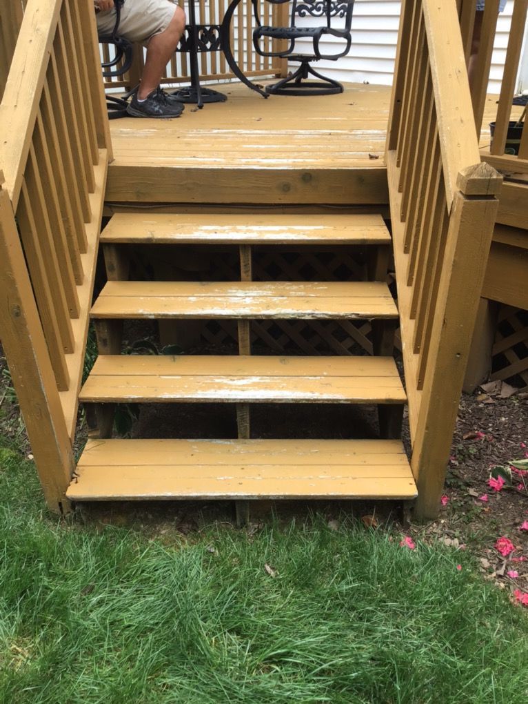 Wooden backyard deck stairs leading up to a patio with chairs, bordered by grass and flowers.