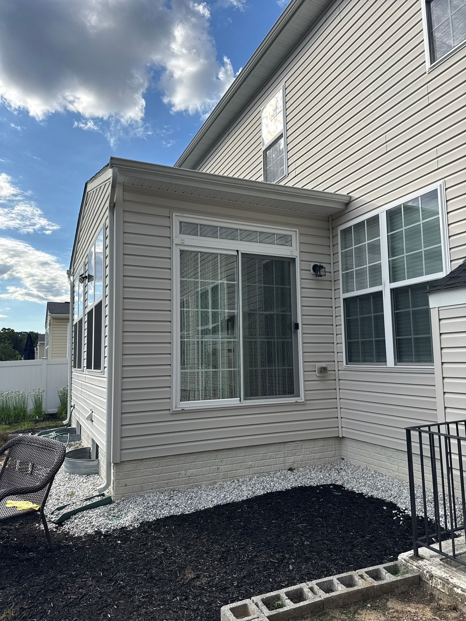 Side of a beige house with a screened porch and sliding glass door under a partly cloudy sky