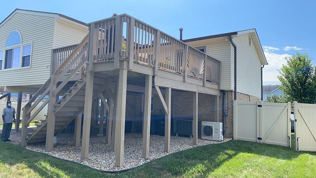 Backyard deck and stairs attached to a beige house, with a fenced yard and lawn.