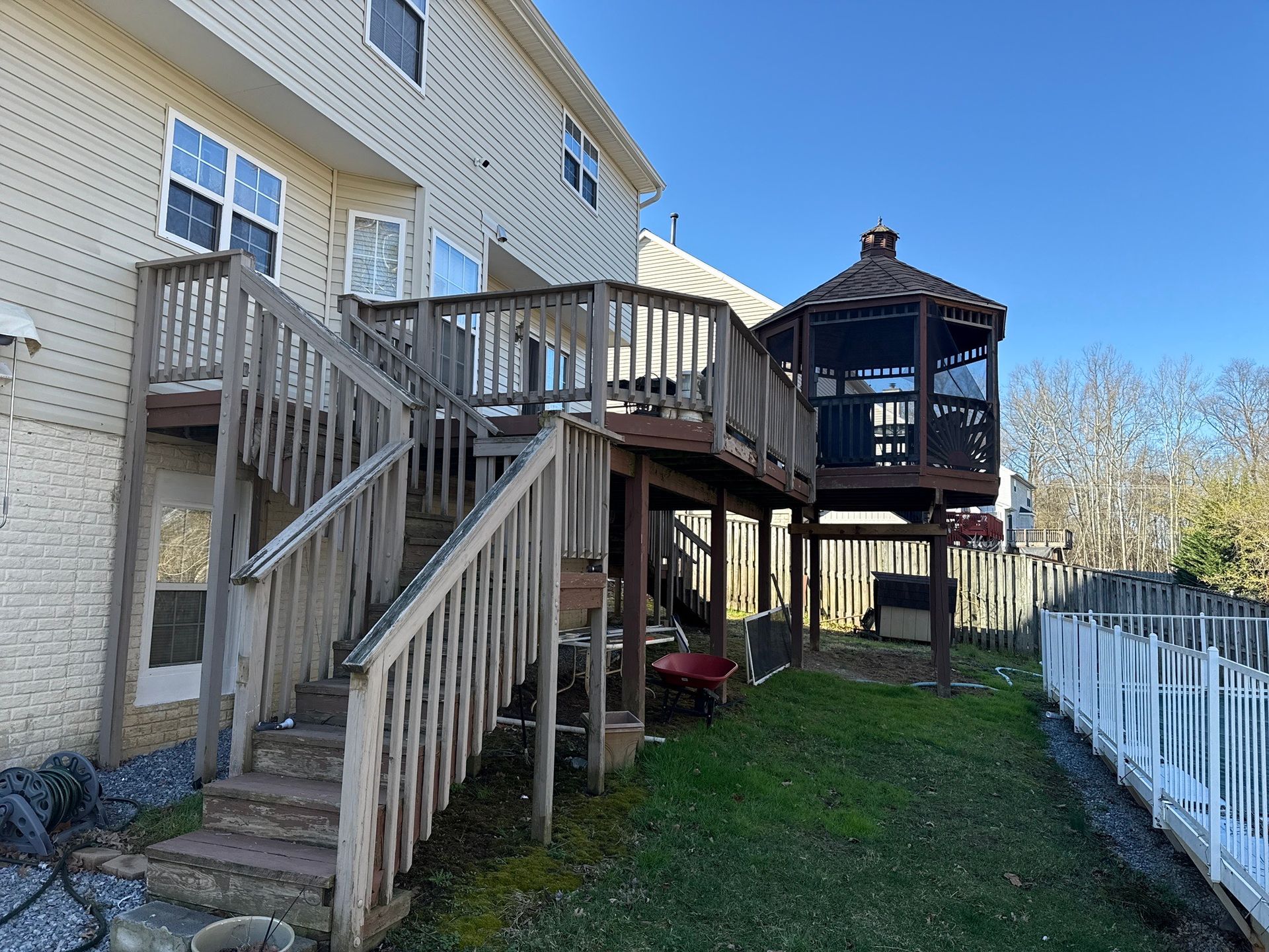 Backyard deck with wooden stairs, gazebo, and white fence beside a brick house