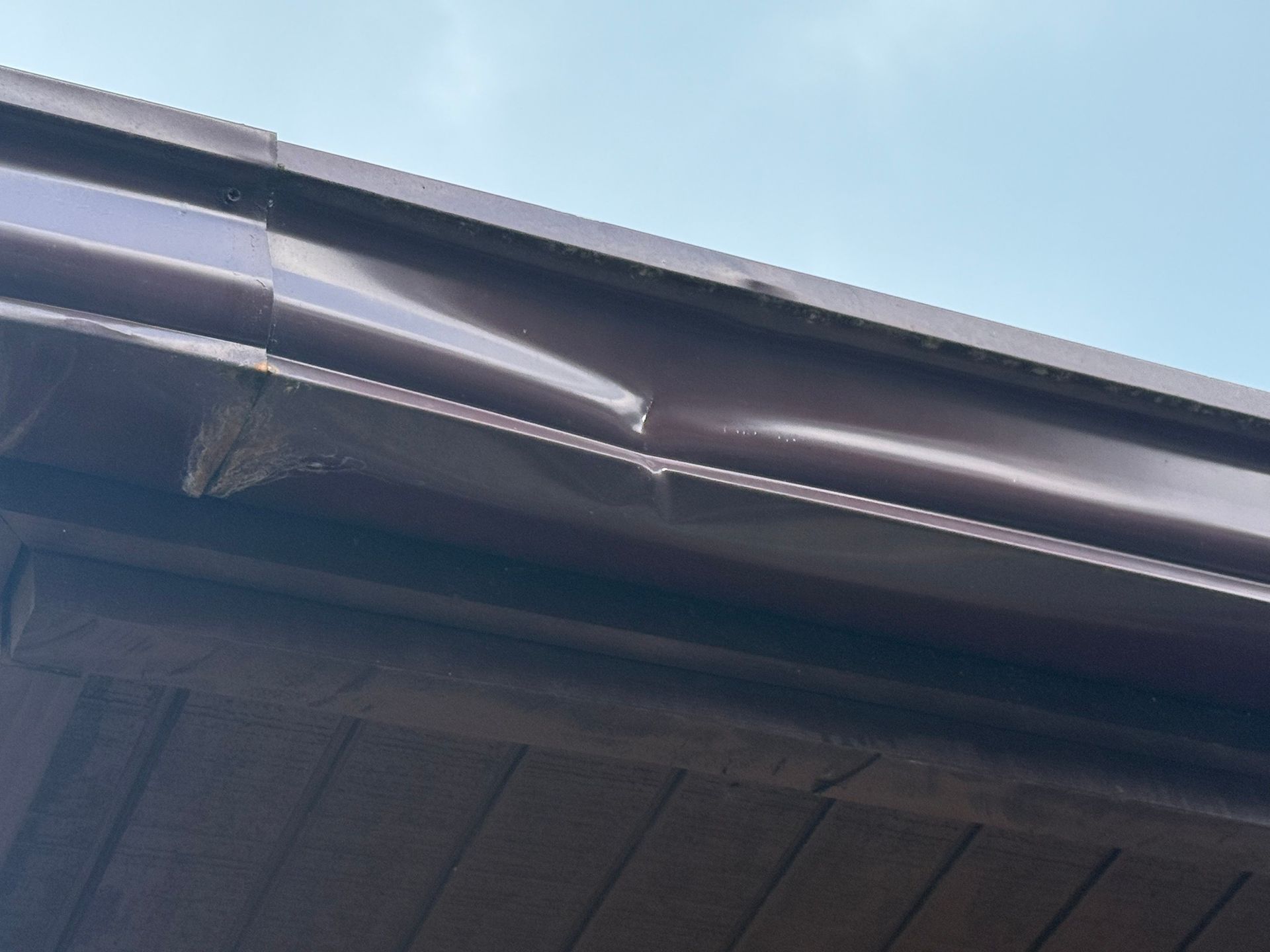 Damaged roof gutter with a large dent against a blue sky