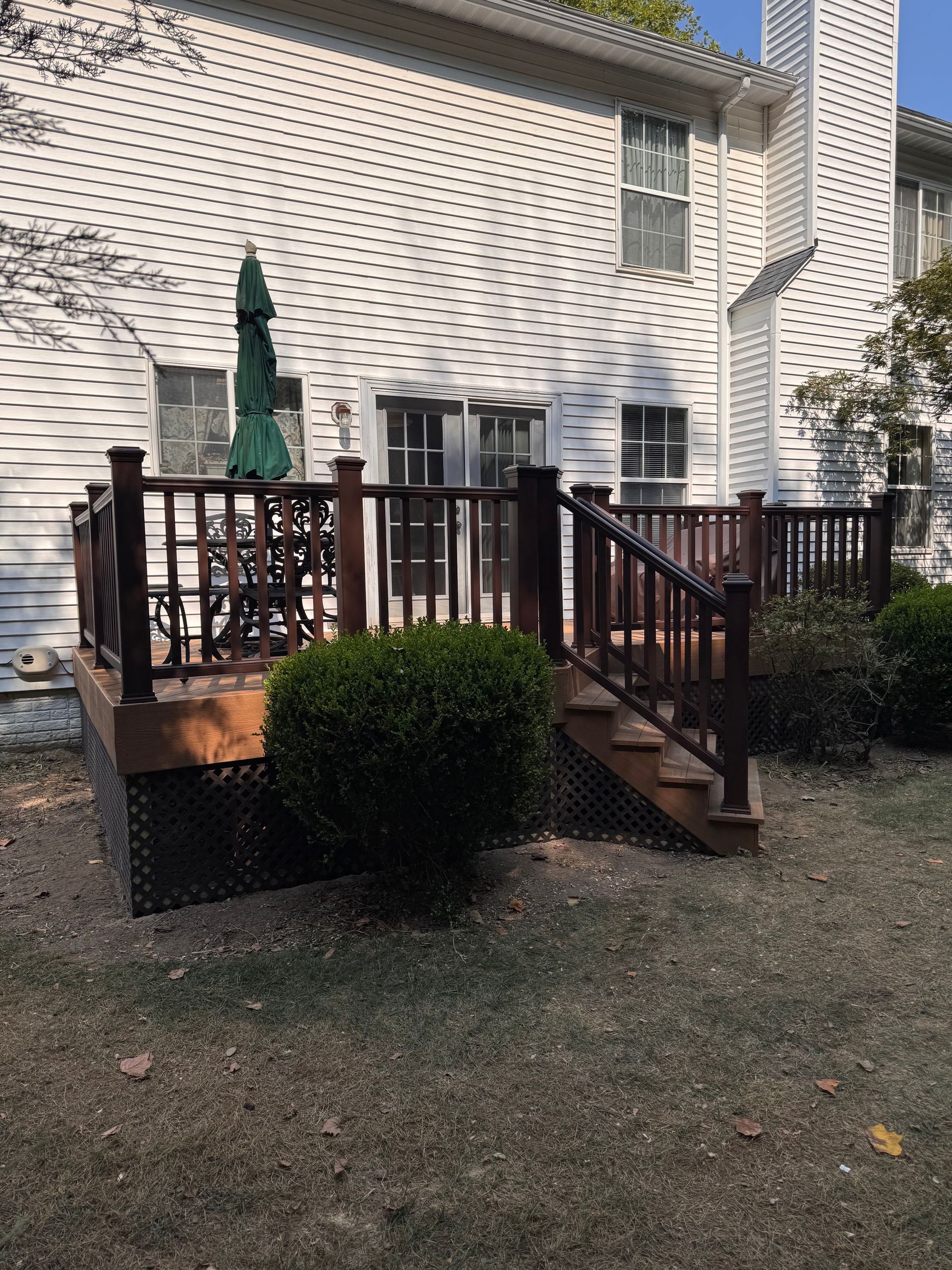 Small wooden deck with stairs and railing in a backyard beside a beige house