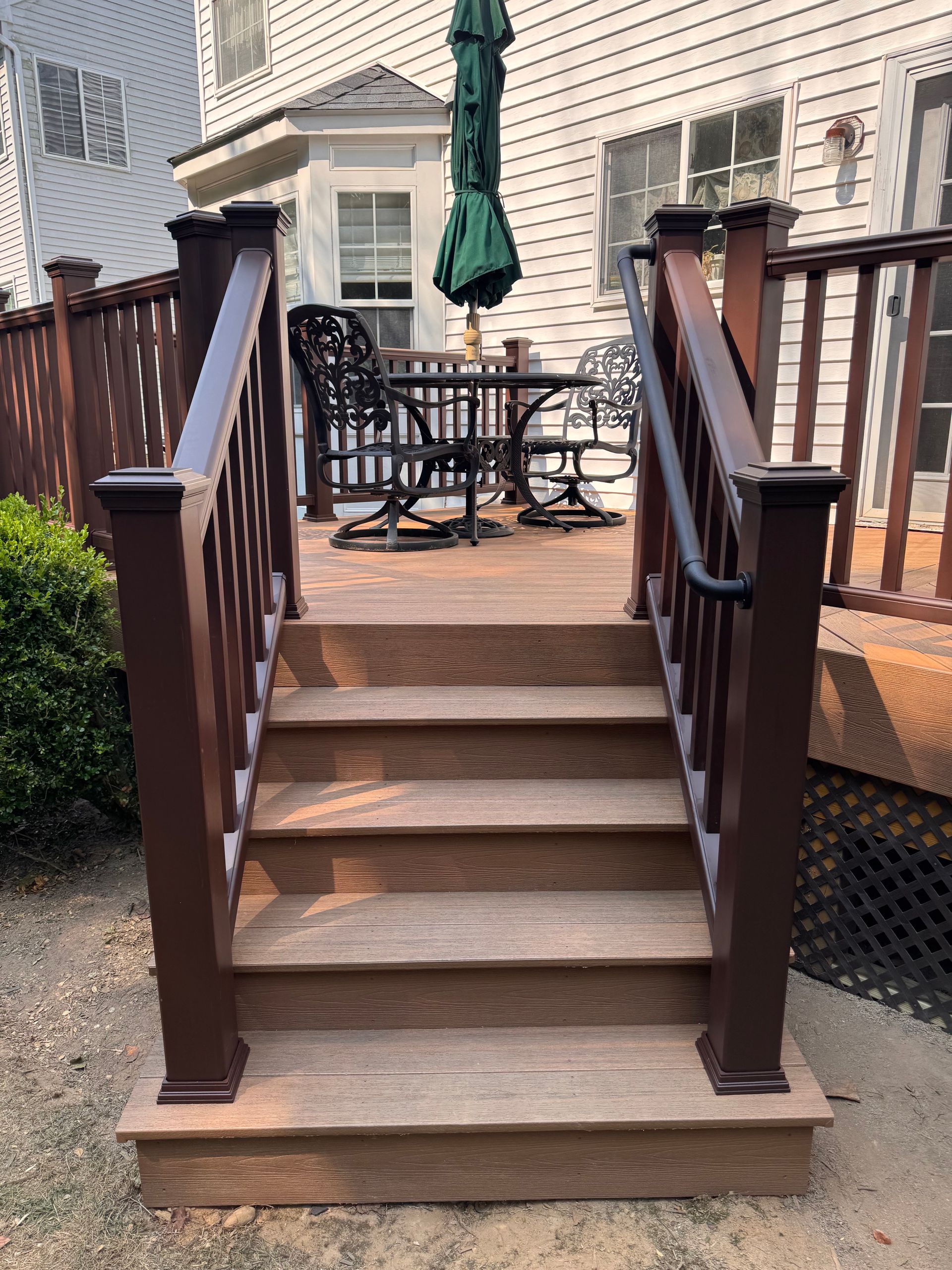 Wooden backyard stairs with railings leading to a patio table and closed green umbrella