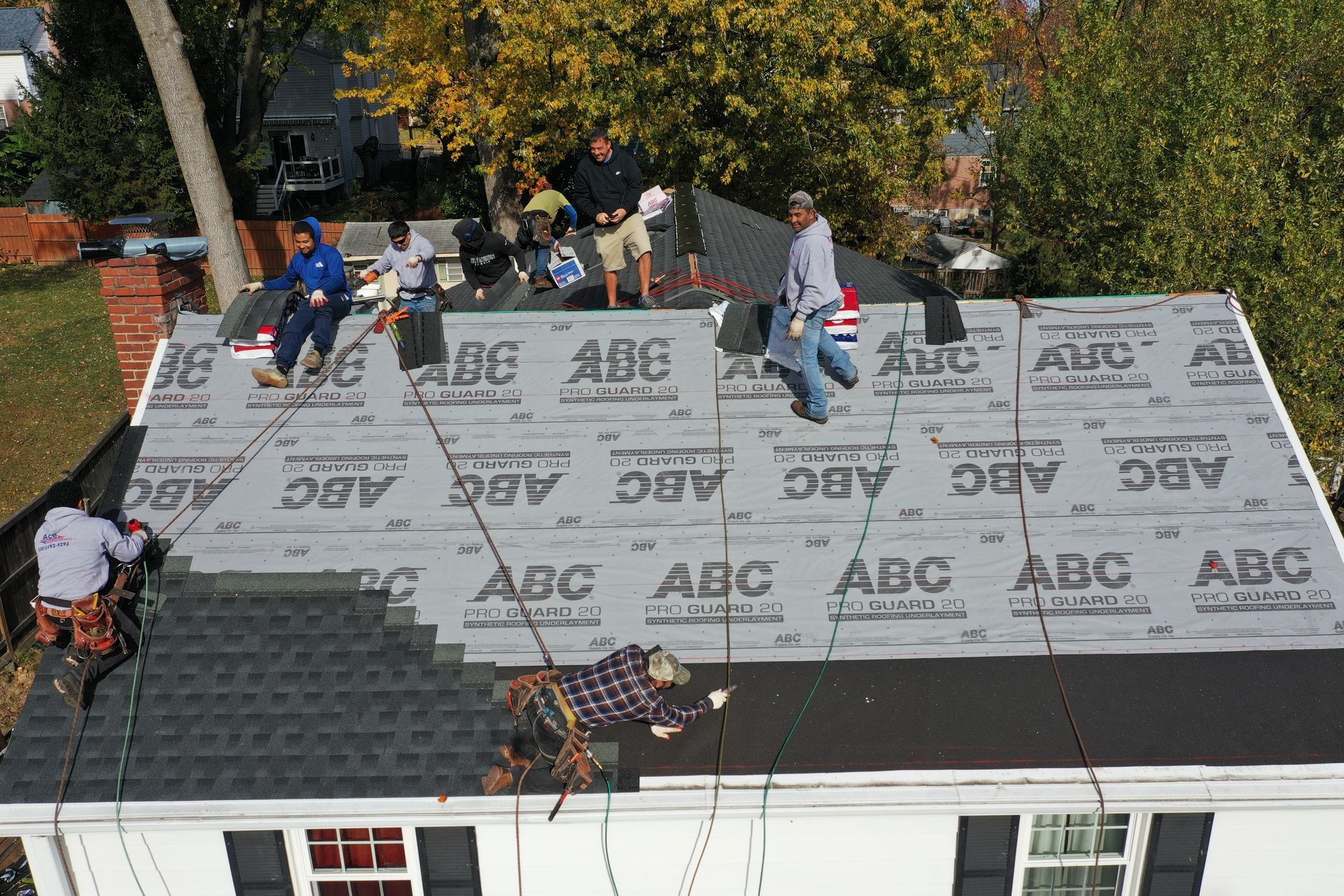 Roofers installing underlayment on a house roof, with tools and materials spread across the shingles.