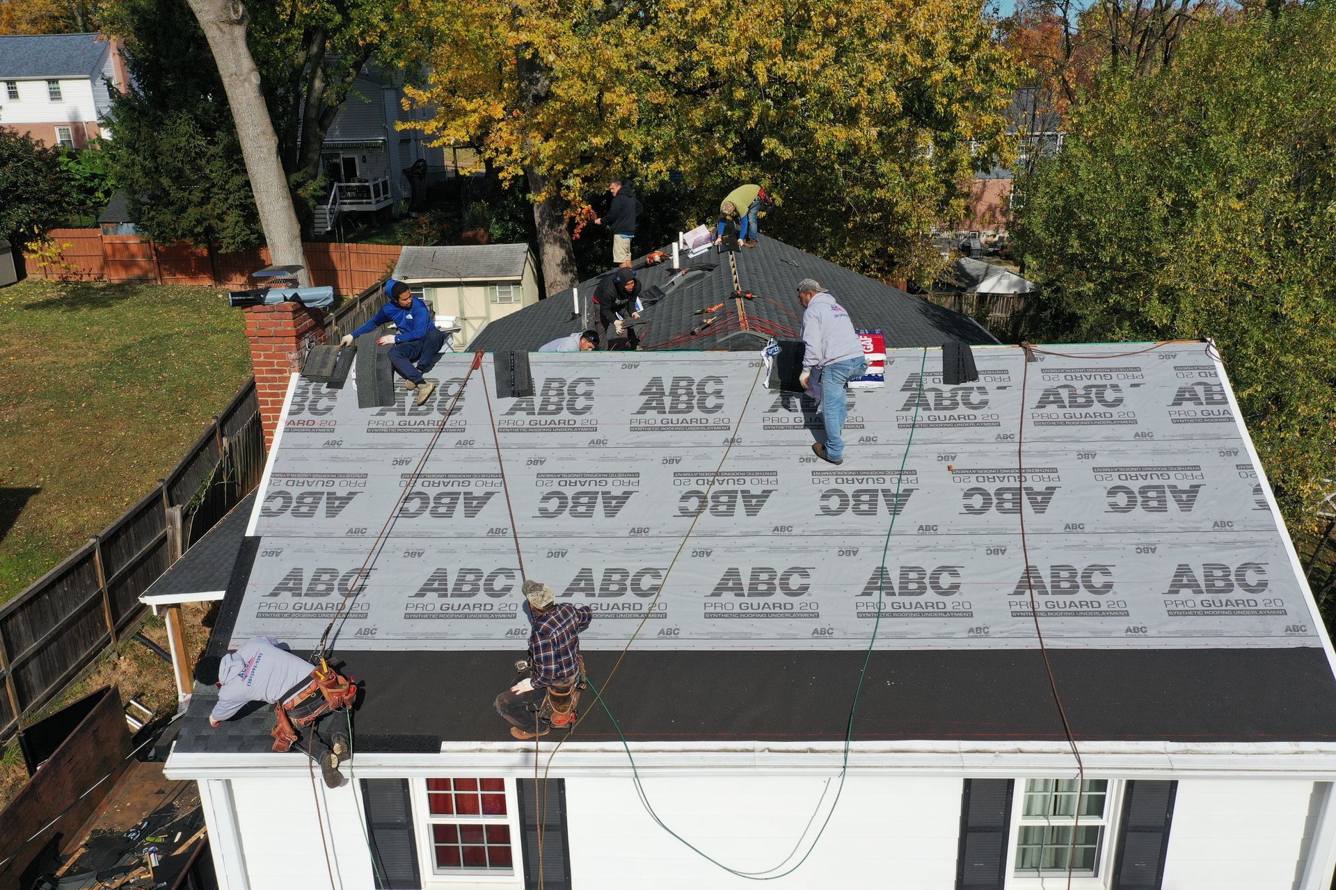 Workers installing roofing on a house with gray underlayment and exposed brick chimneys