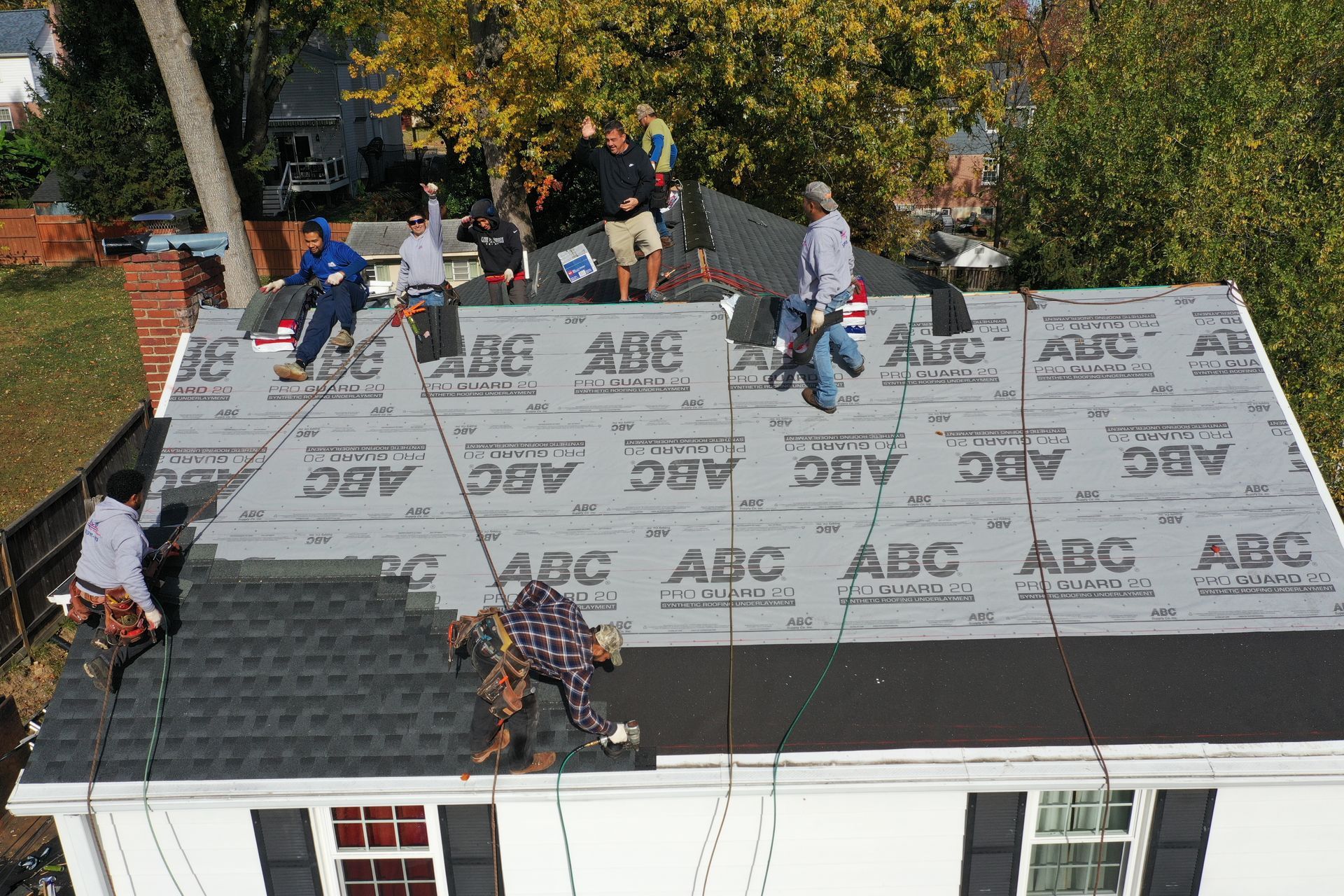 Roofers installing gray shingles on a house roof, with workers and materials spread across the roof.