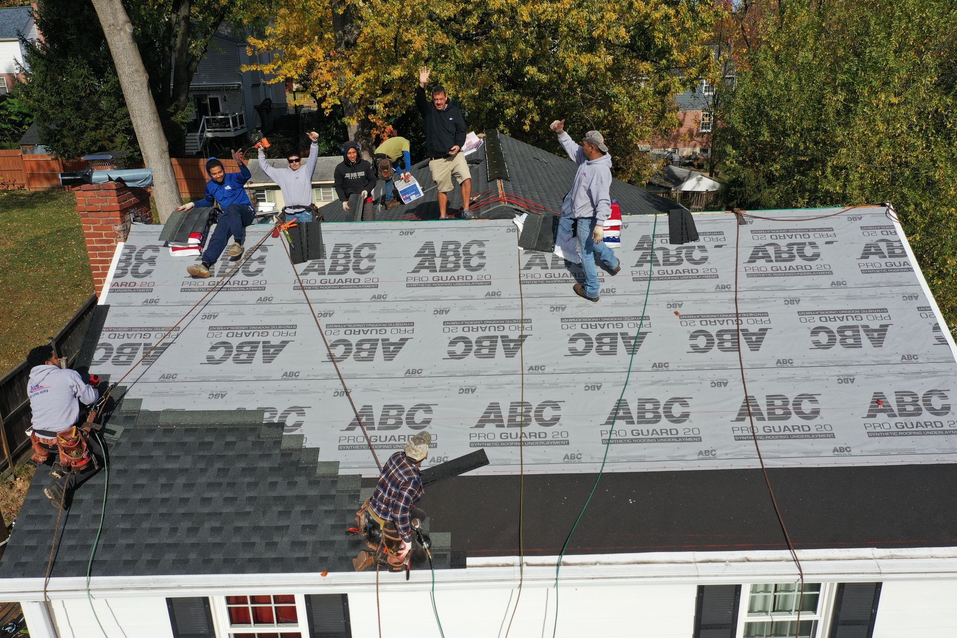 Workers installing roofing on a house, with bundled materials and fall protection on the roof.