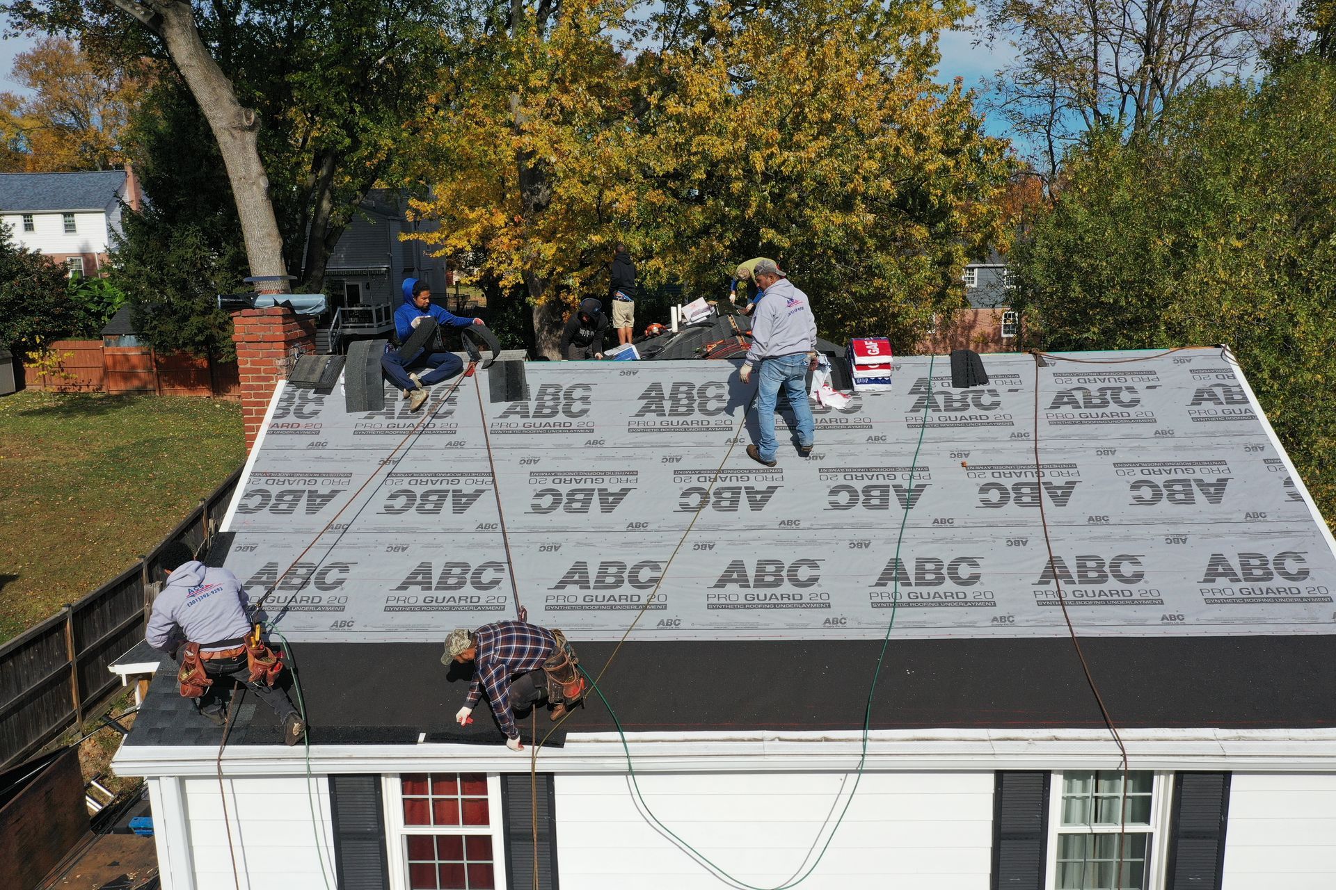 Workers installing roofing underlayment on a house roof on a sunny day