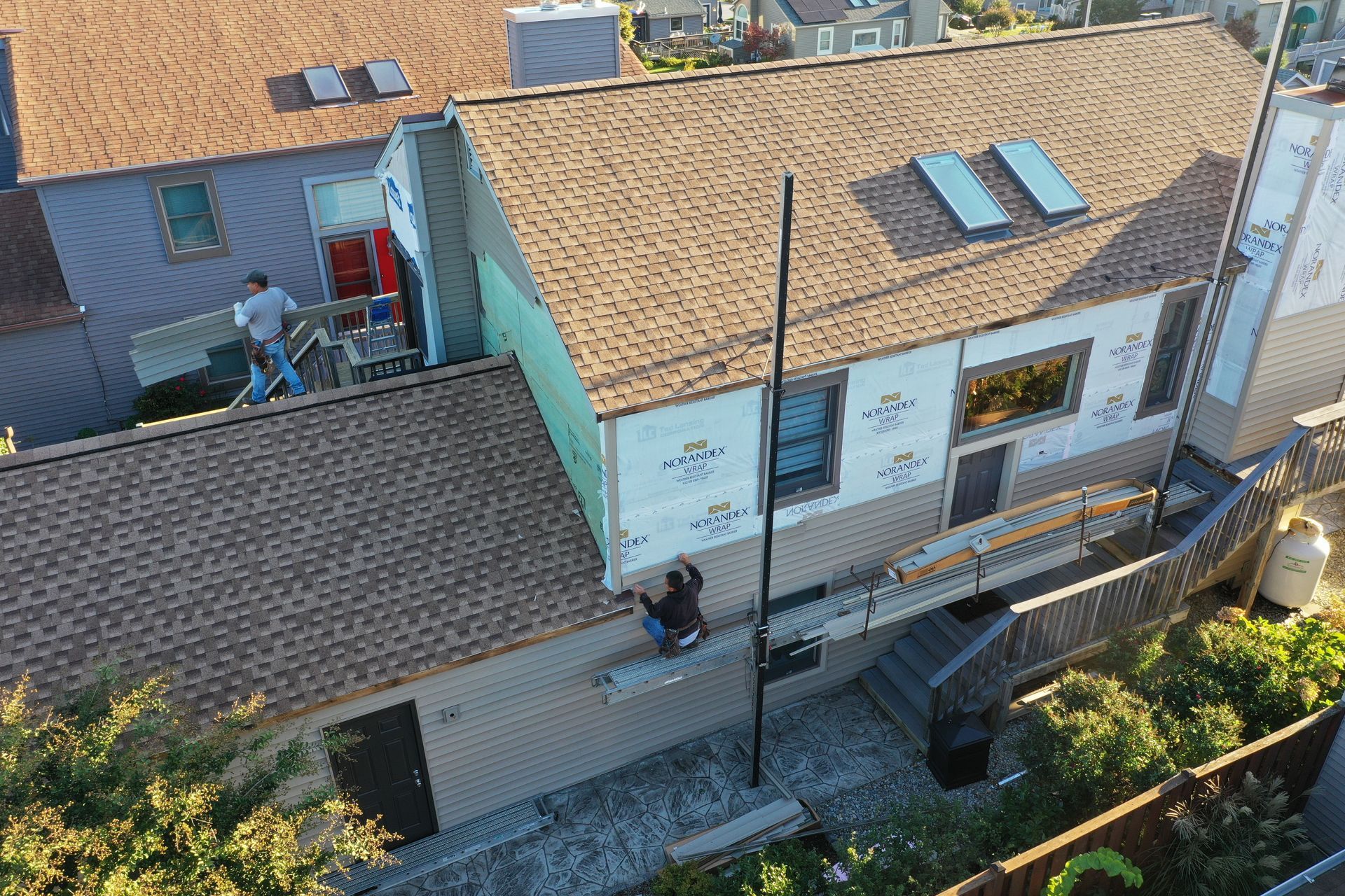 Aerial view of a white house with a tan roof, skylights, and a person standing by the side door.