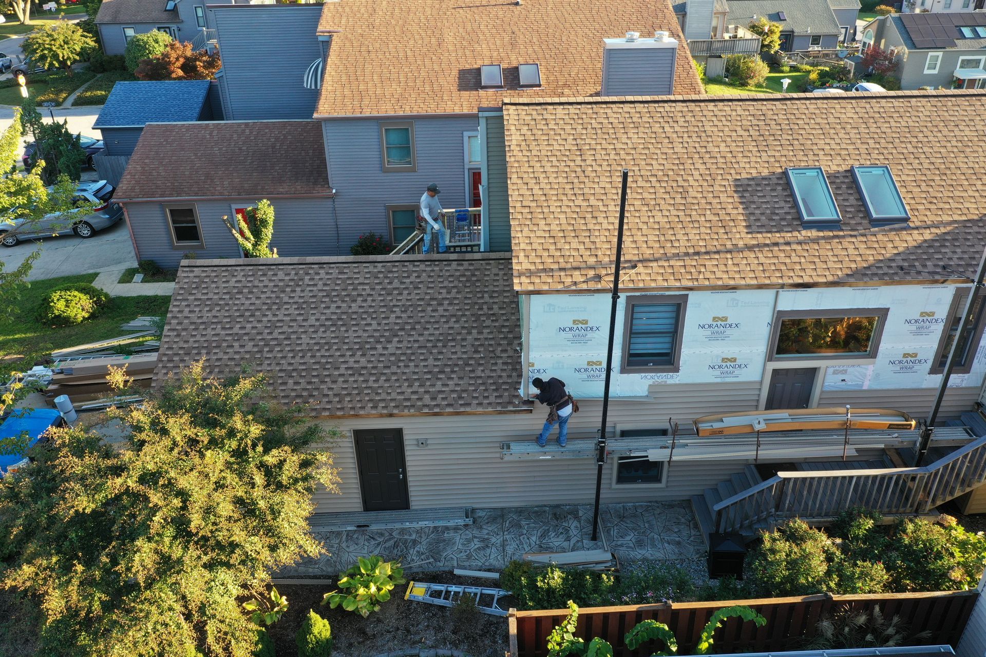 Aerial view of suburban rooftops and a backyard patio with two people working outdoors.