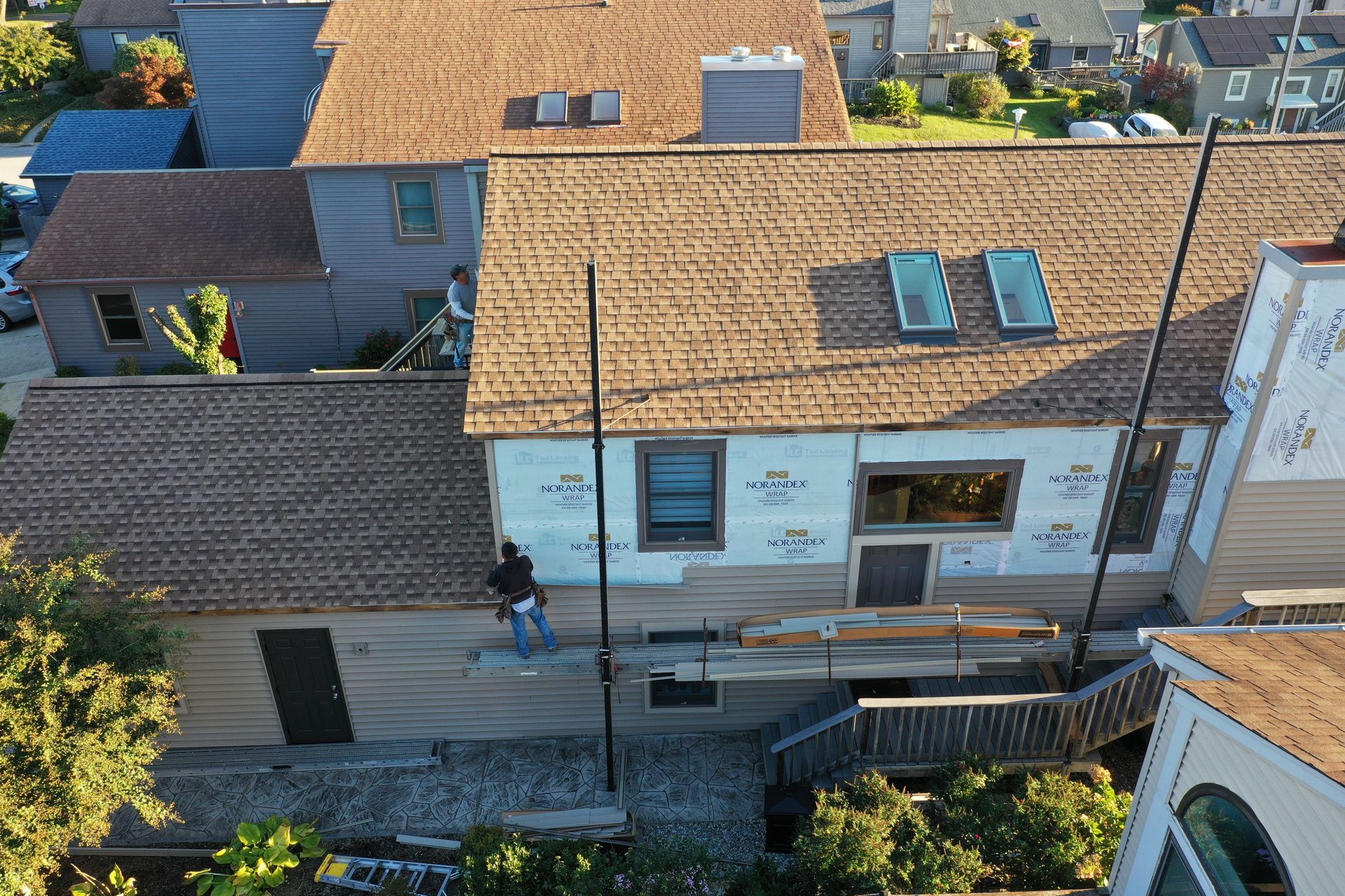 Aerial view of a residential street with houses, tiled roofs, and a person walking beside a white building.