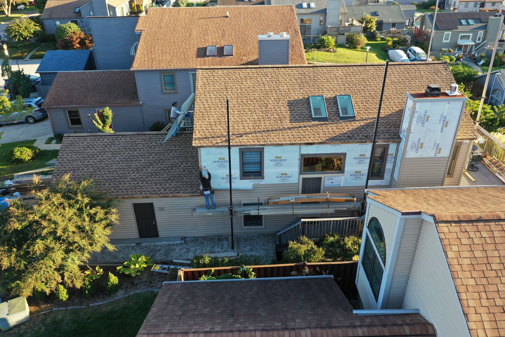 Aerial view of a row of tan-roofed houses with skylights and rooftop solar panels in a residential neighborhood