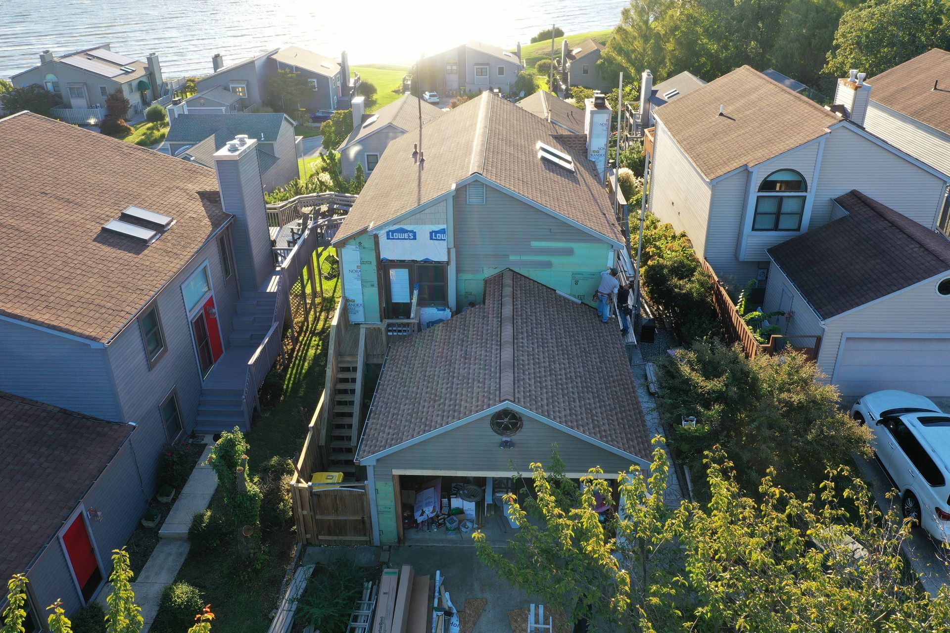 Aerial view of a narrow residential alley with small houses, parked cars, and trees in bright sunlight