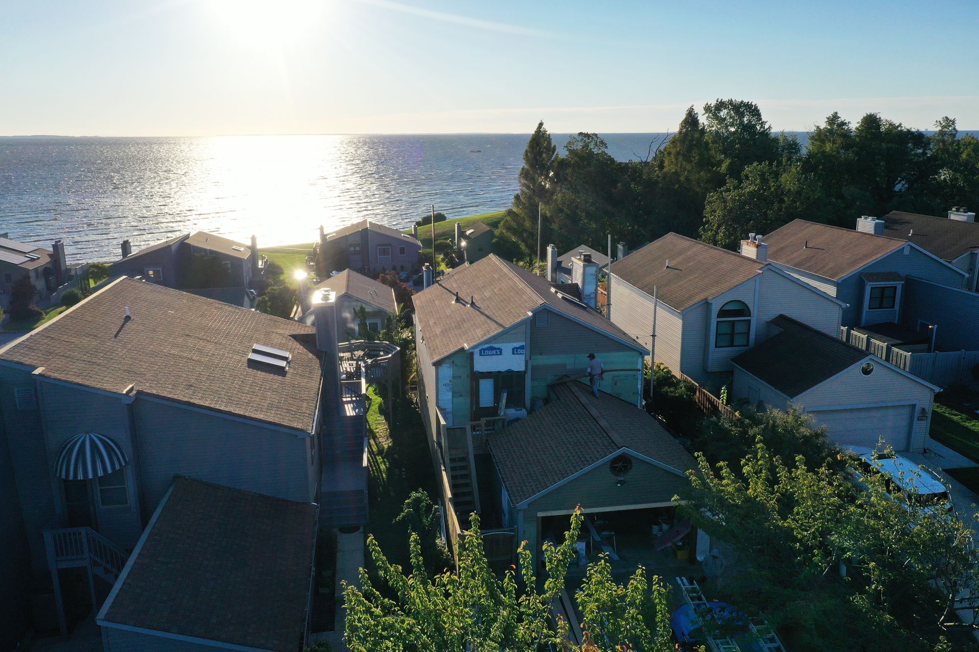 Sunlit coastal neighborhood with rooftops, trees, and the ocean at sunset