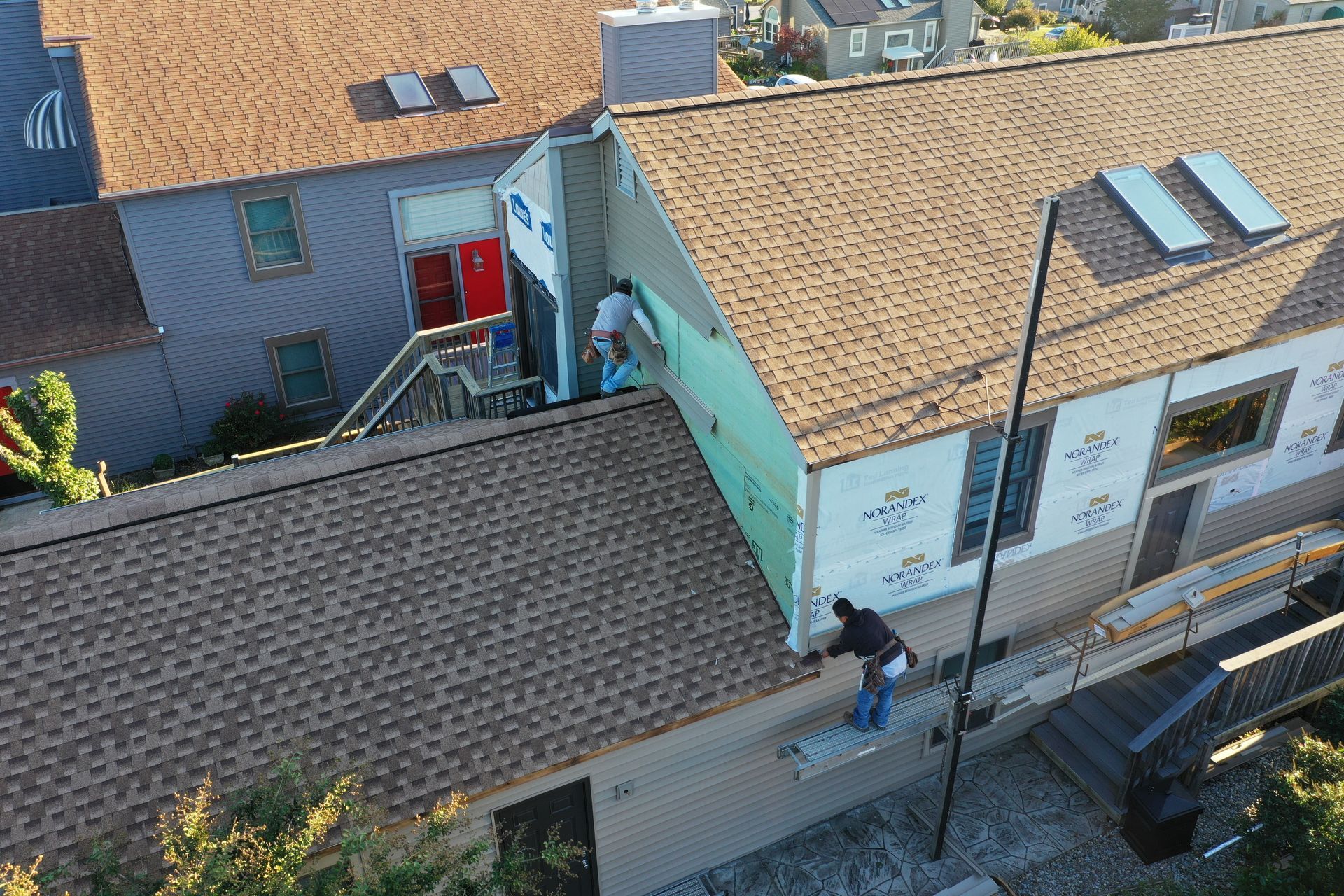 Overhead view of workers on a rooftop beside a turquoise building with red doors and skylights