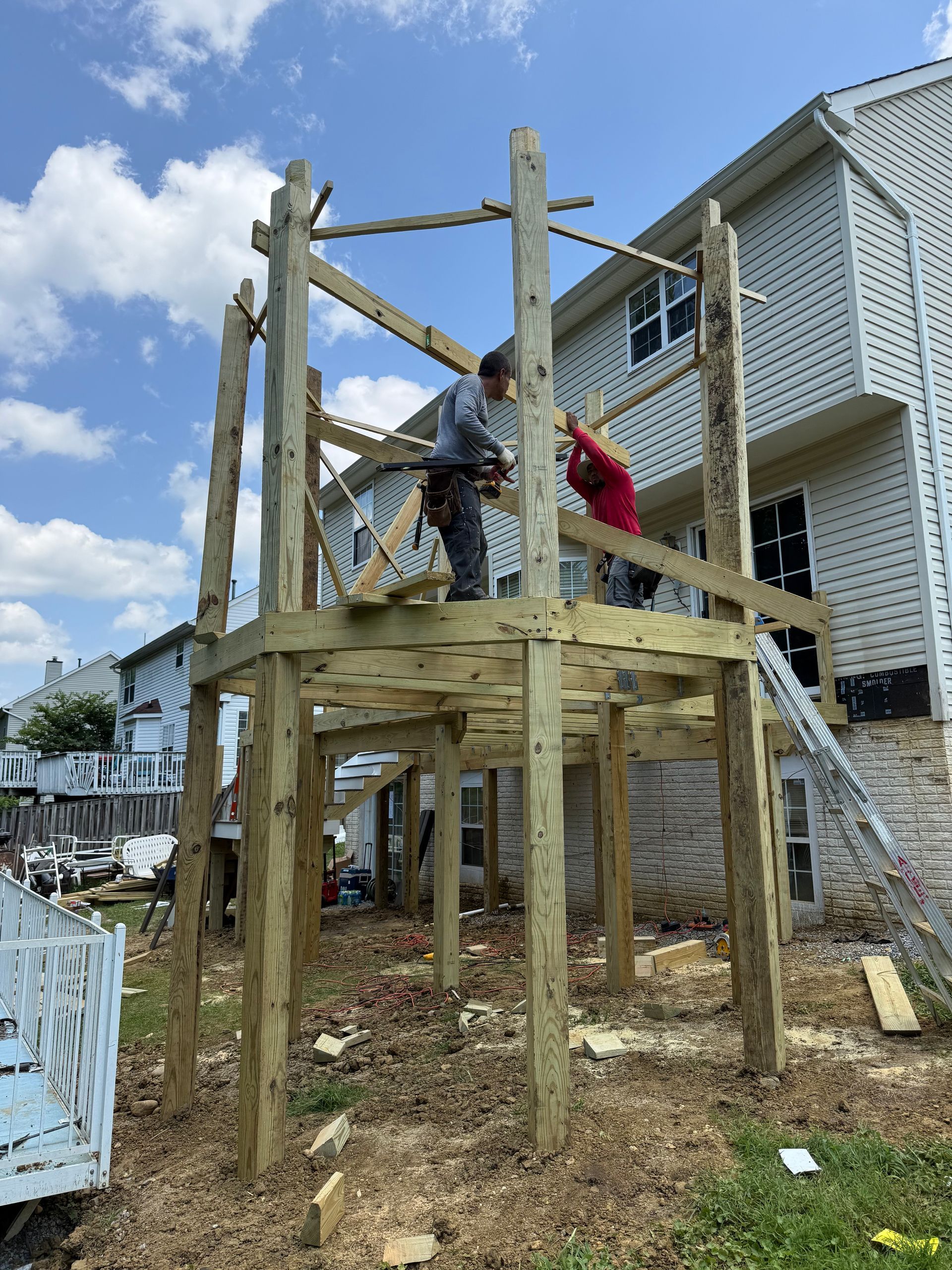 Workers building a wooden deck frame beside a white house on a hillside