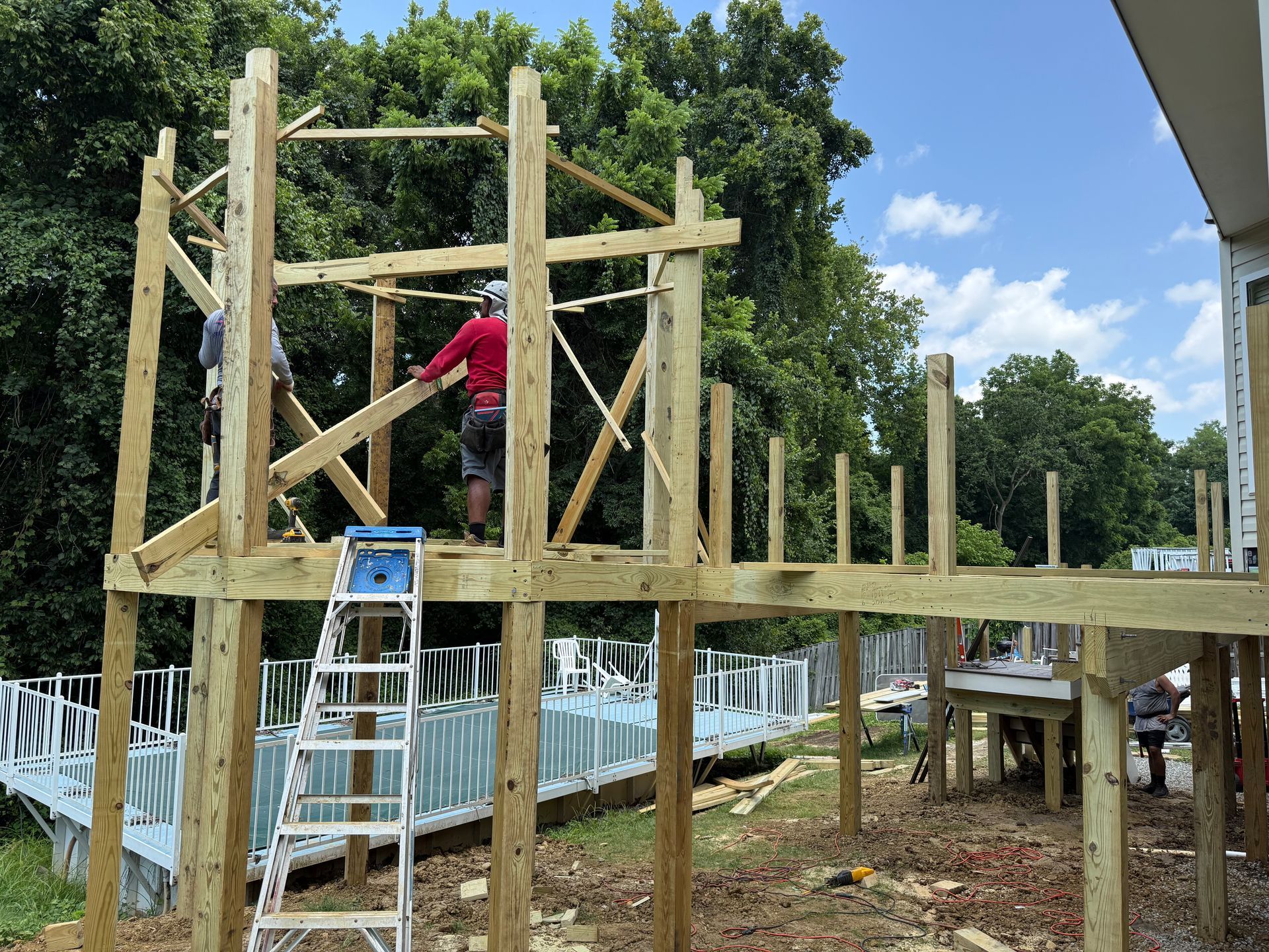 Person on a ladder building a wooden deck frame beside a house under construction