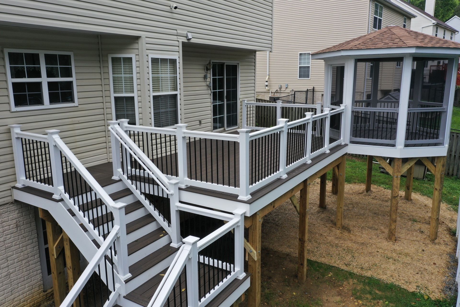 Wooden deck and stairs leading to a screened gazebo beside a beige house