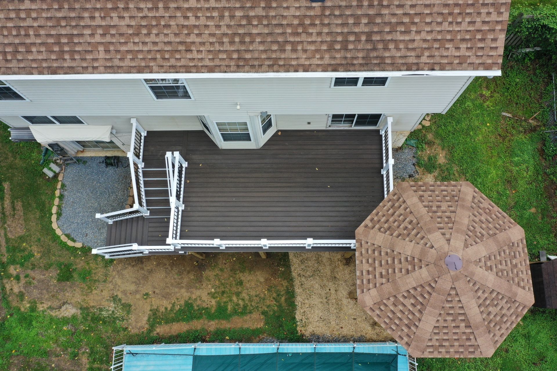 Aerial view of a house deck with white railing and a large tan patio umbrella beside a grassy yard.