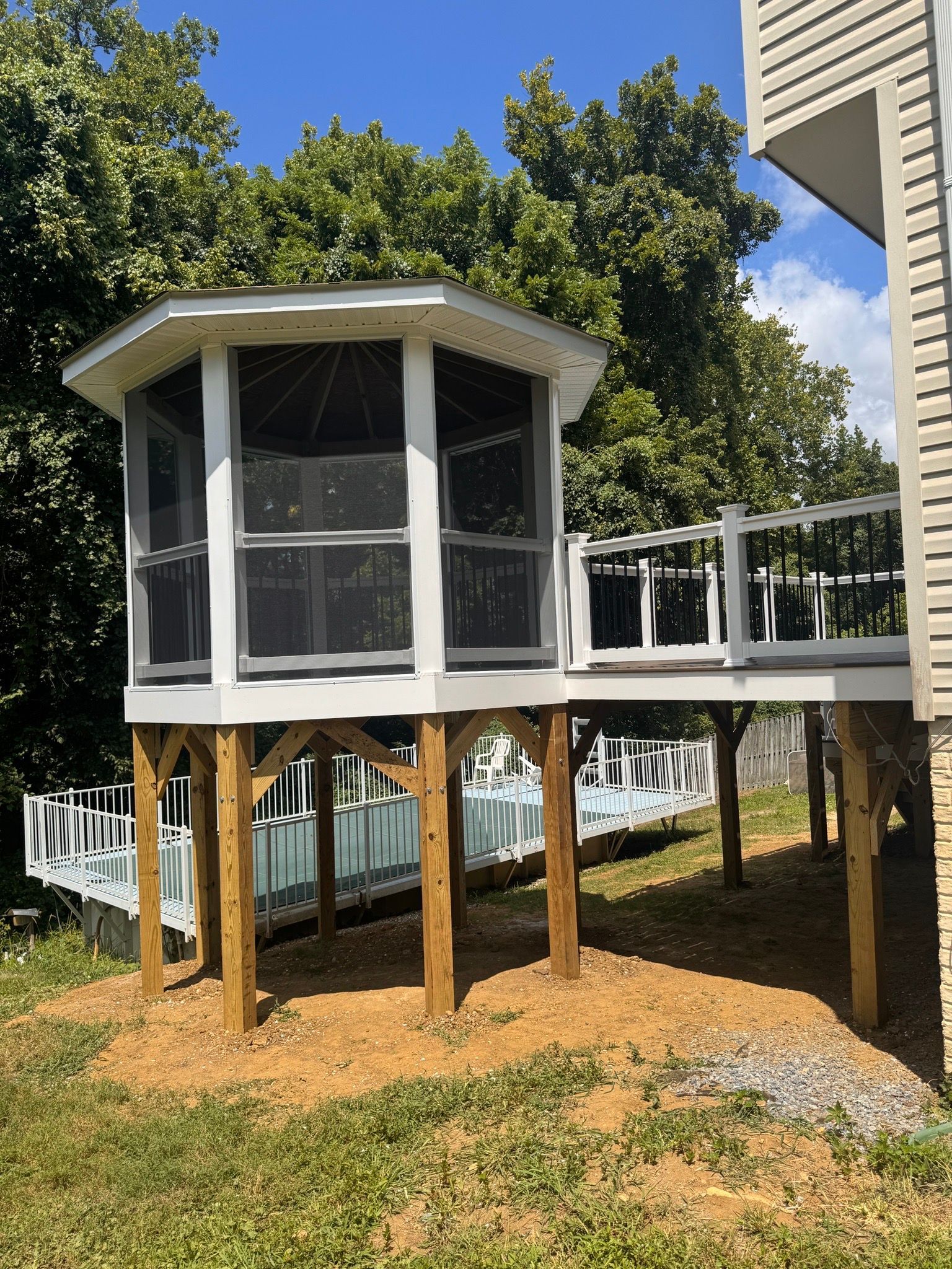 Raised screened porch with white railings and tan supports in a leafy backyard.