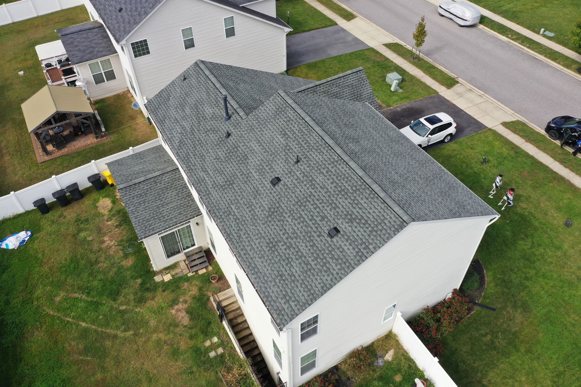 Aerial view of a white house with a gray roof, driveway, parked cars, and green lawn.