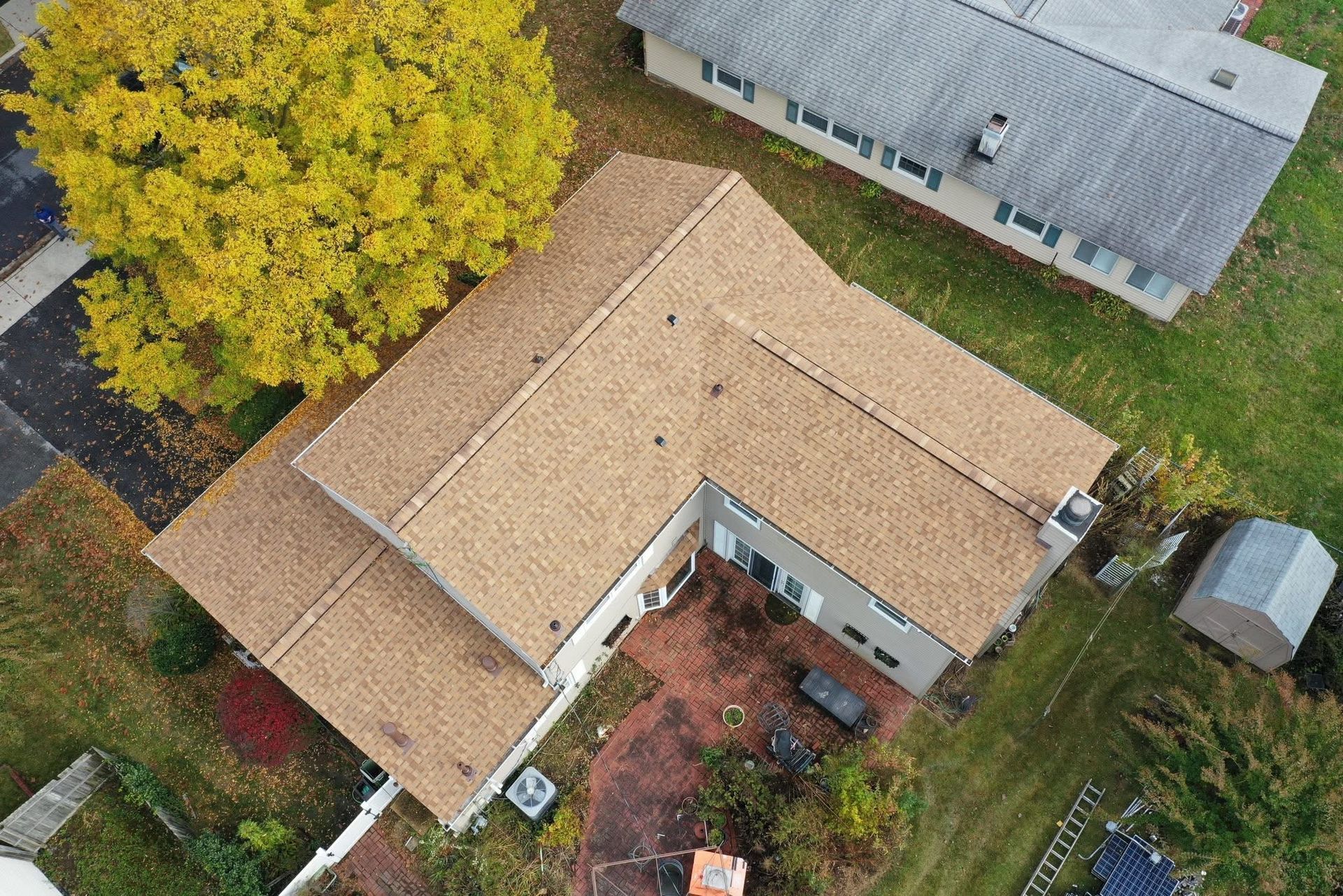 Aerial view of a tan-roofed house beside a large yellow tree and lawn.