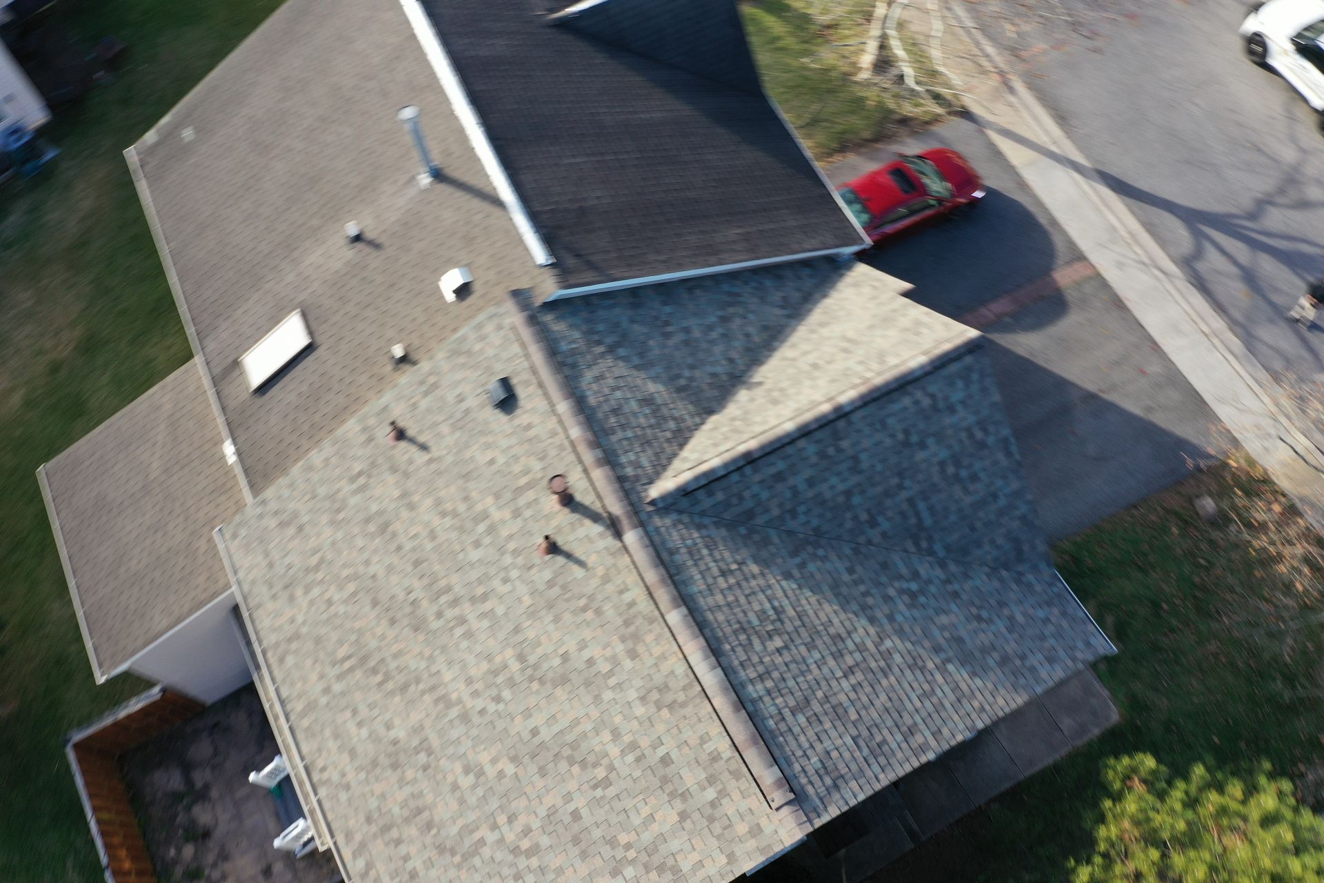Aerial view of a suburban house roof with a red car parked beside the driveway.