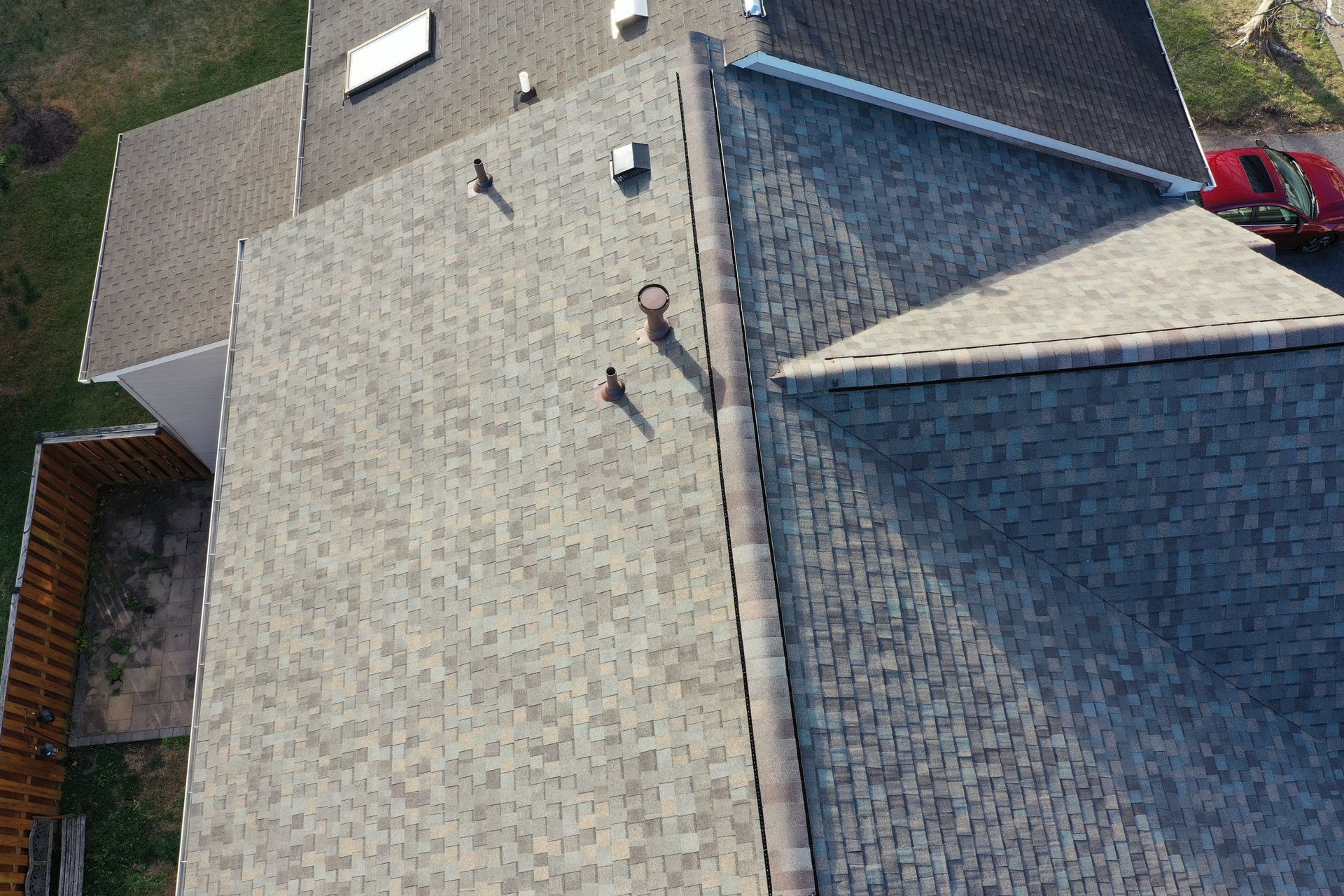 Aerial view of a house roof with gray shingles, vents, and a red vehicle at the edge.