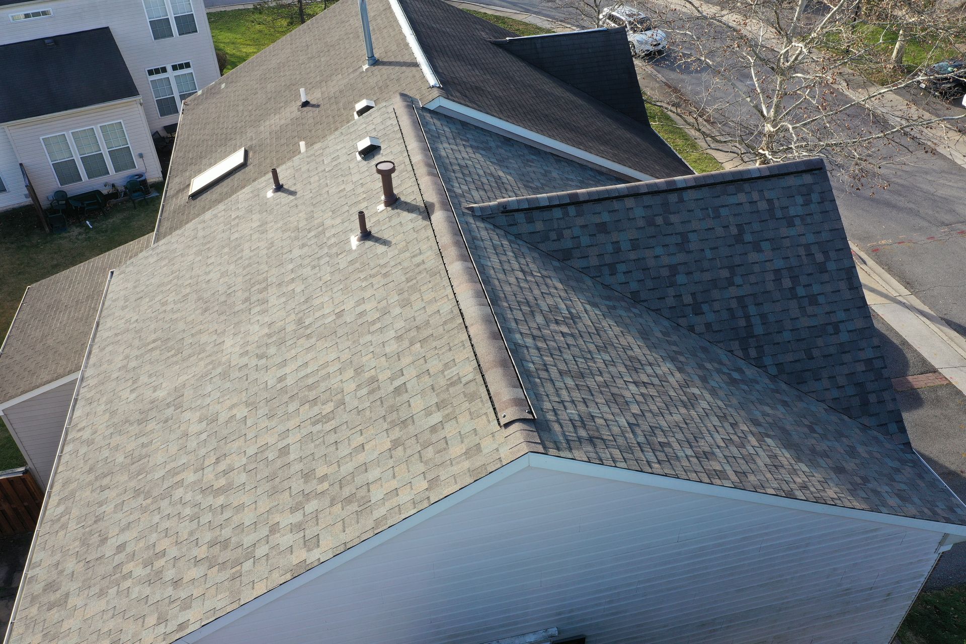 Aerial view of a residential roof with gray shingles and several vents next to neighboring houses.