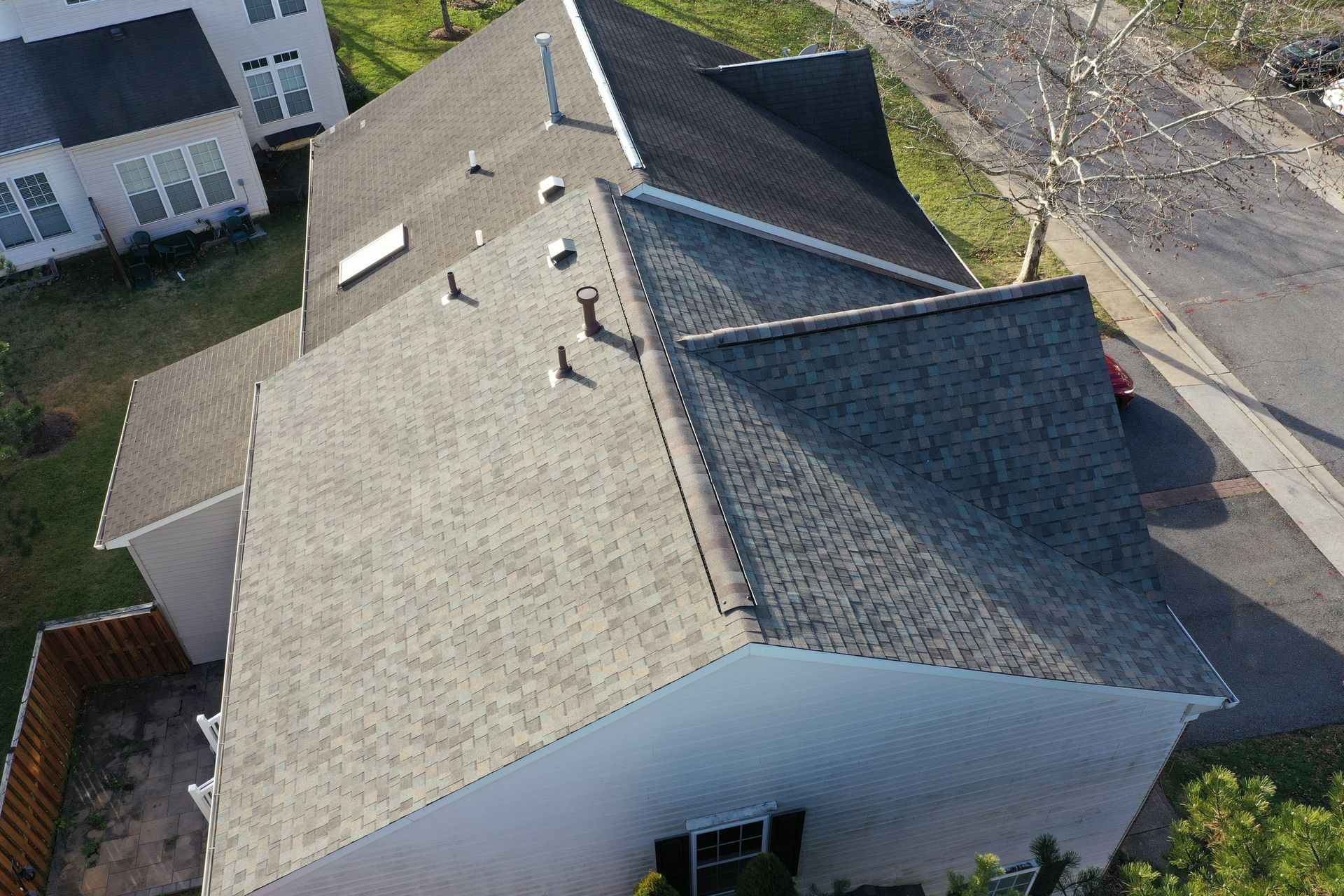 Aerial view of a gray shingled house roof with skylights and a driveway beside it