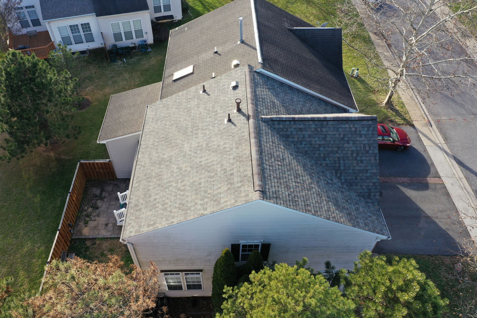 Aerial view of a suburban house with a gray roof, driveway, and surrounding trees.