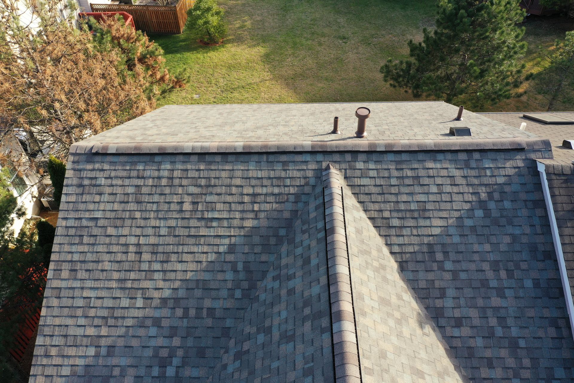 Aerial view of a shingled roof with a ridge vent and trees in the background.