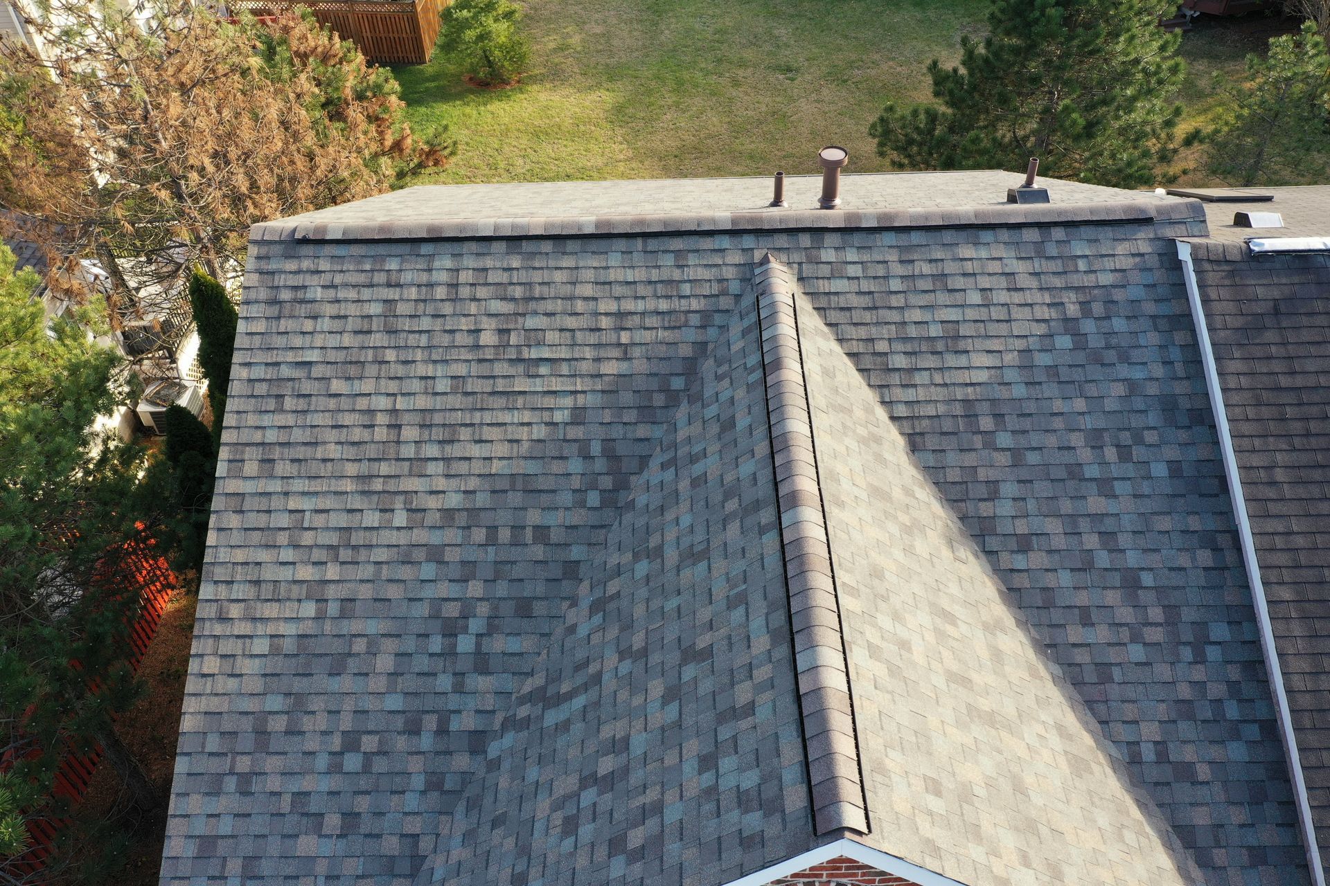 Aerial view of a gray shingled roof with a triangular dormer and trees nearby