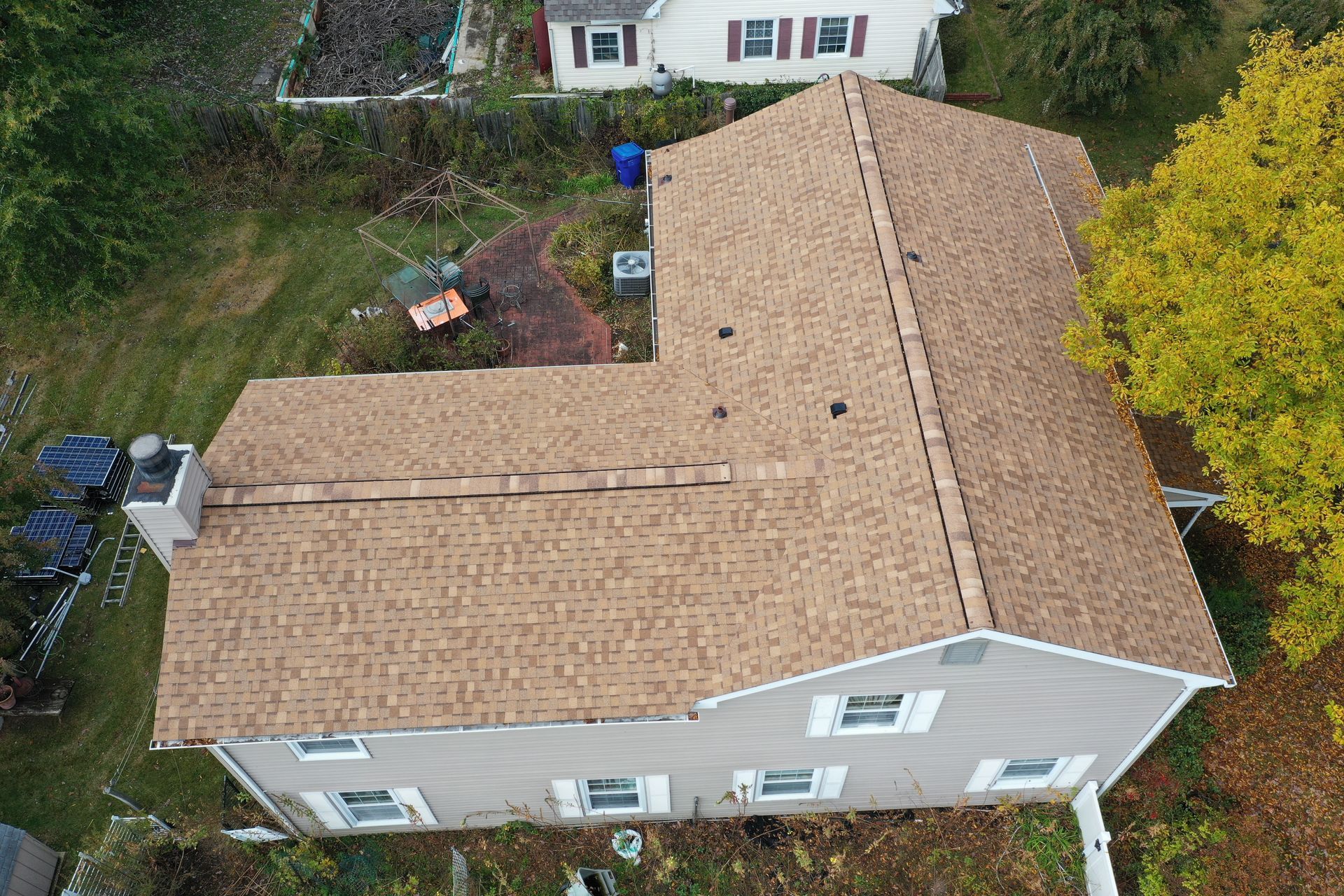 Aerial view of a tan shingle-roof house with a gray exterior and surrounding trees.