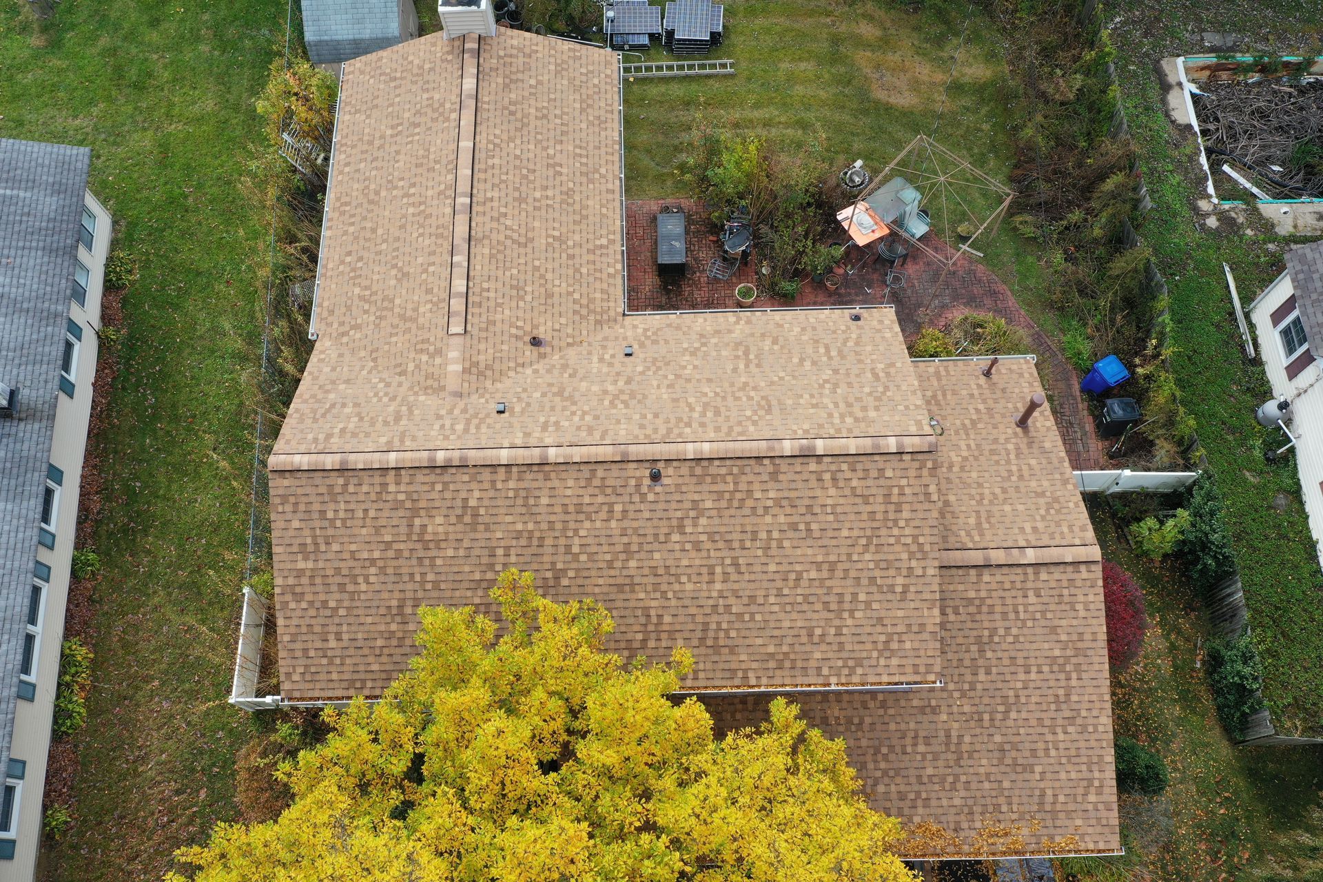 Aerial view of a tan-roofed house with a small backyard and surrounding trees.