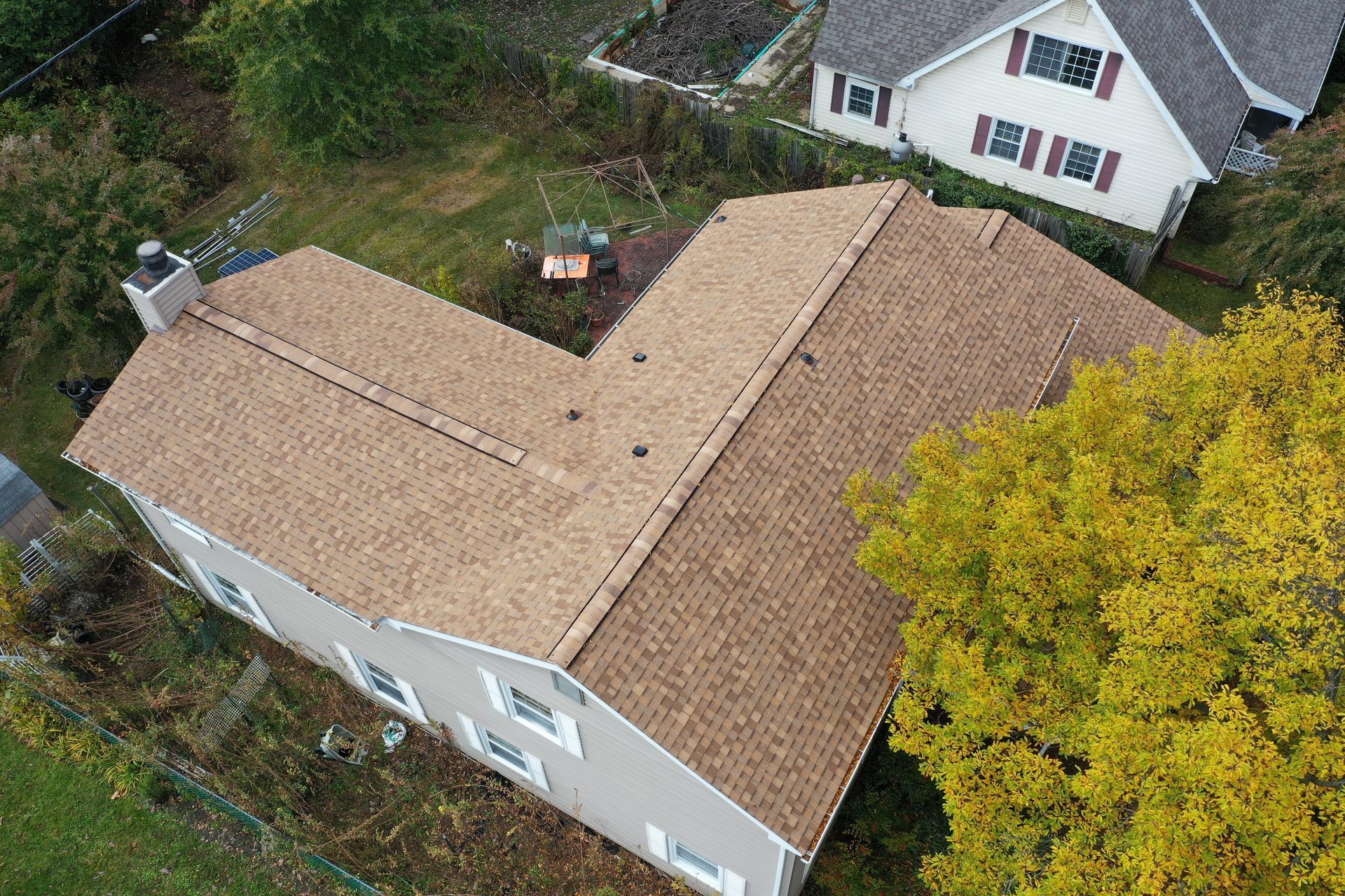 Aerial view of a tan shingle roof with a white house and yellow tree beside it