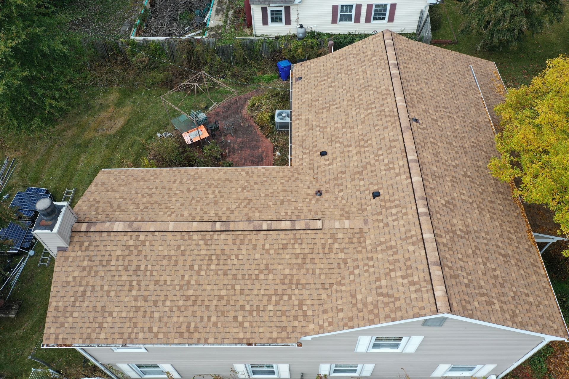Aerial view of a tan shingled roof with a brick chimney and backyard below
