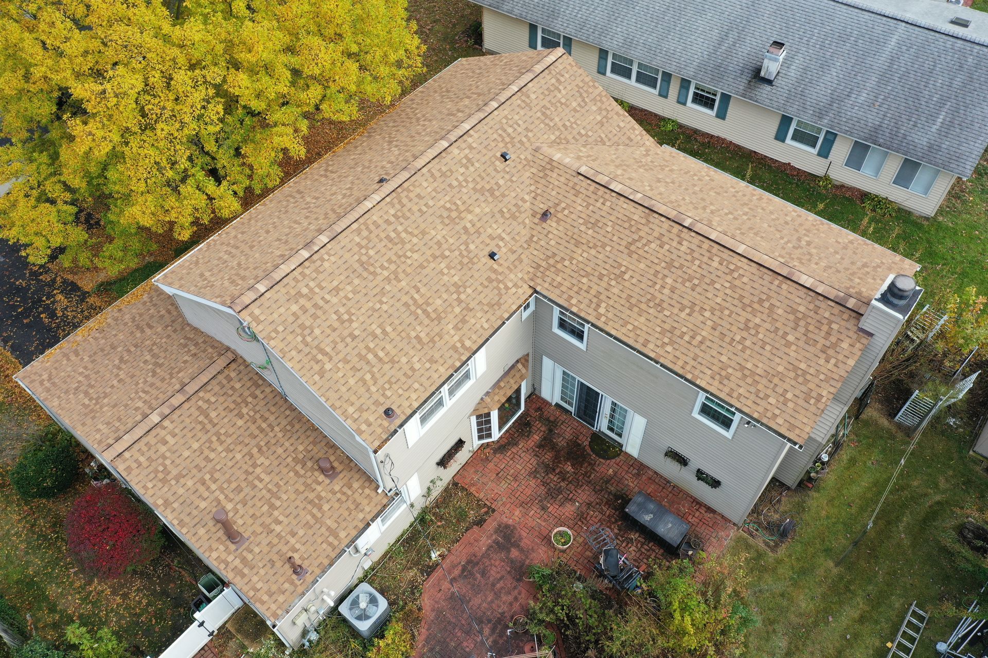 Aerial view of a tan-roofed suburban house with a small backyard and surrounding trees