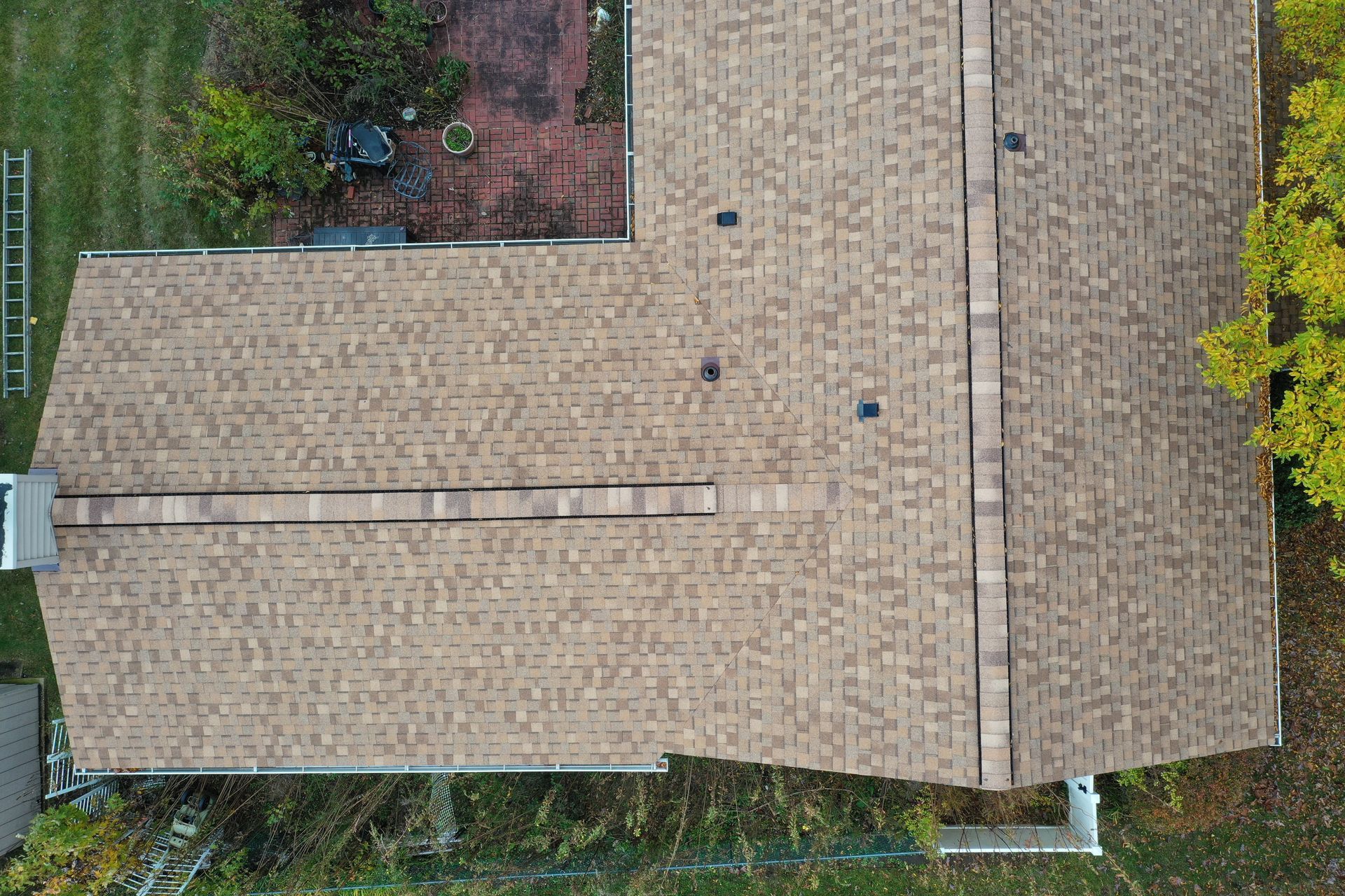 Aerial view of a tan shingled roof with a narrow skylight strip, bordered by trees and garden.