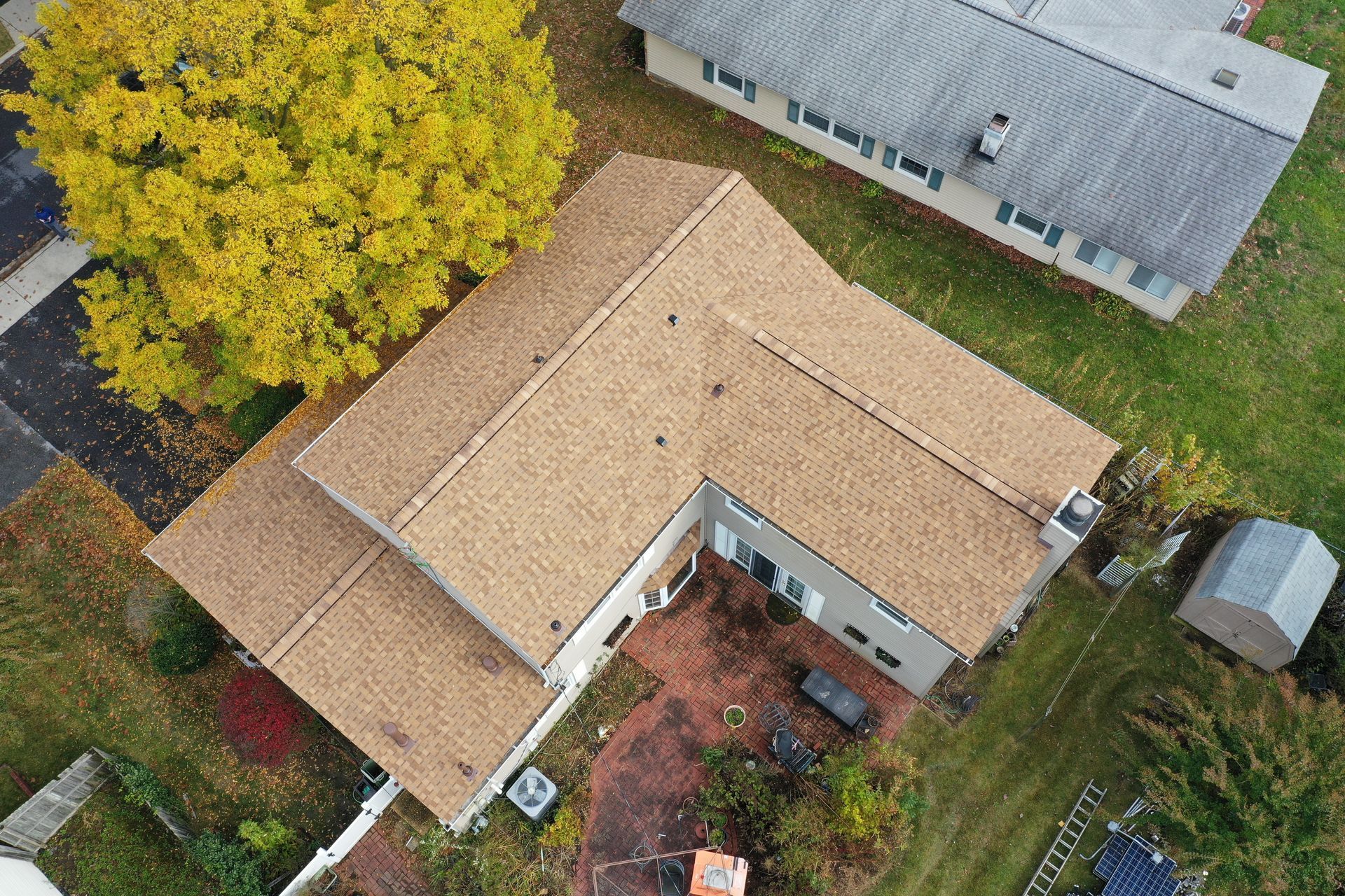 Aerial view of a tan-roofed house beside a large yellow tree and a red patio area.