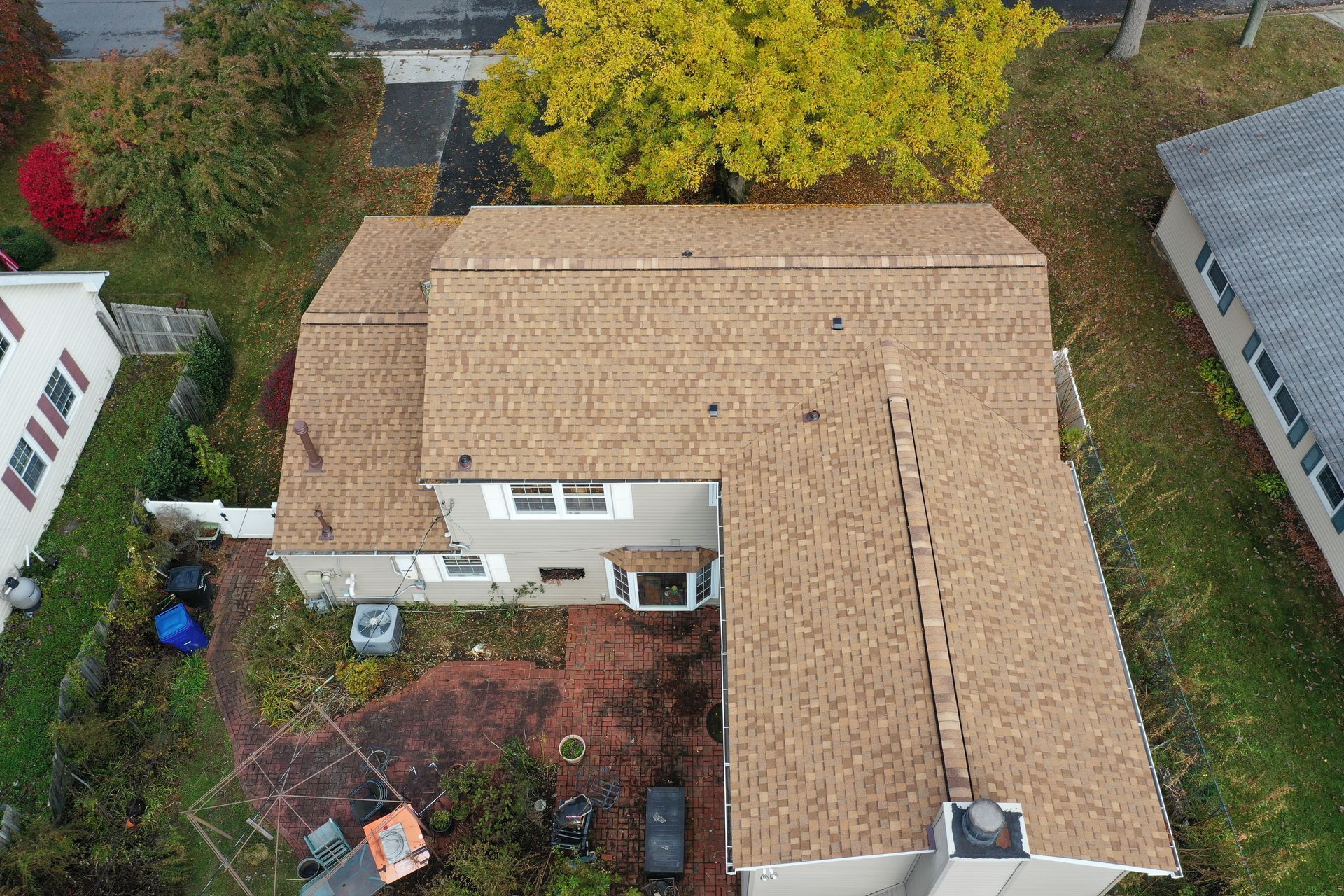 Aerial view of a tan-roofed house with a fenced backyard and autumn trees nearby